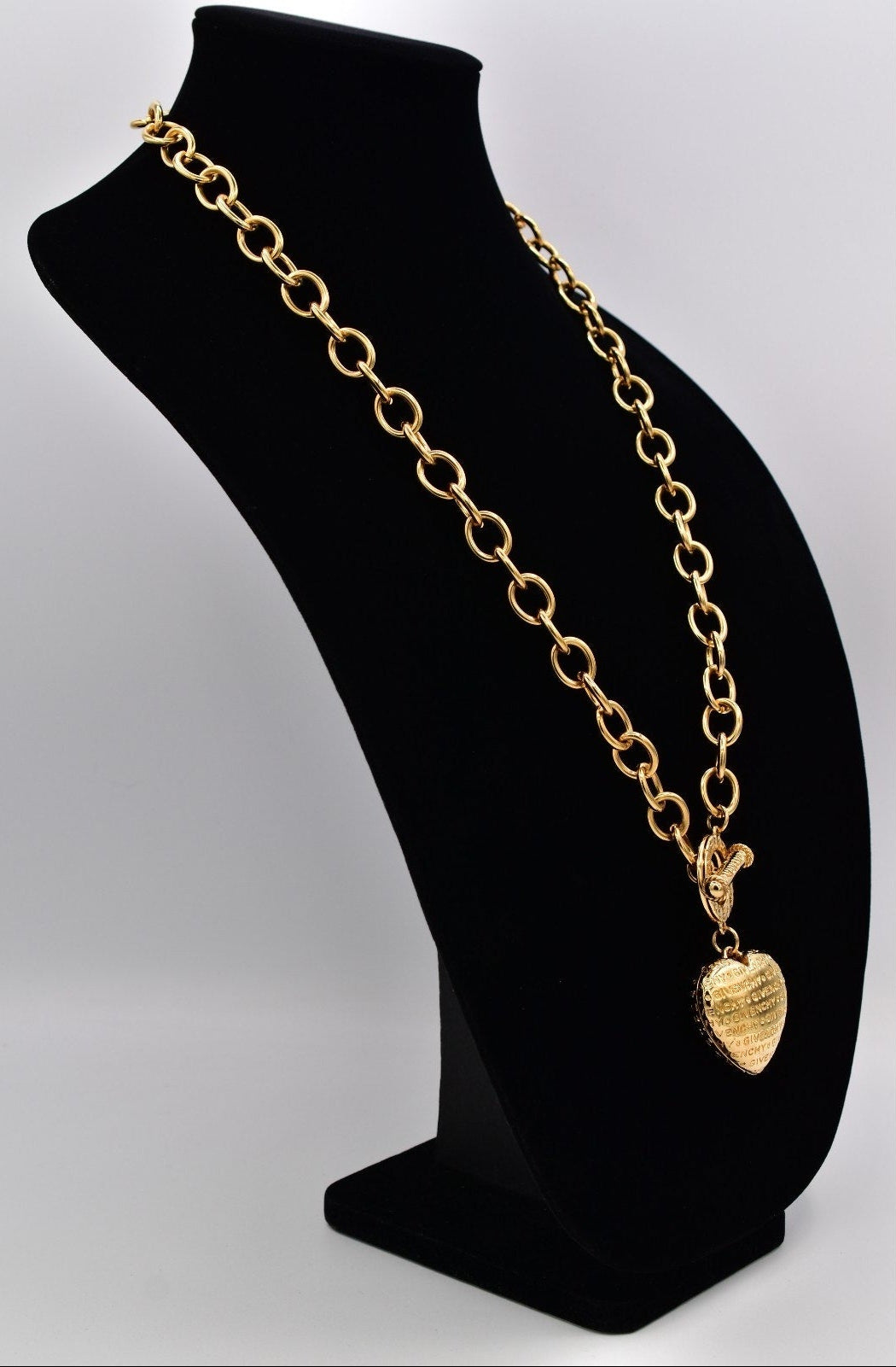 Gold chain necklace with a heart pendant on a black mannequin bust.