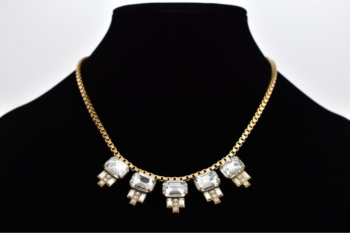 A gold chain necklace with five rectangular clear rhinestone clusters, displayed on a black velvet jewelry bust against a white background.