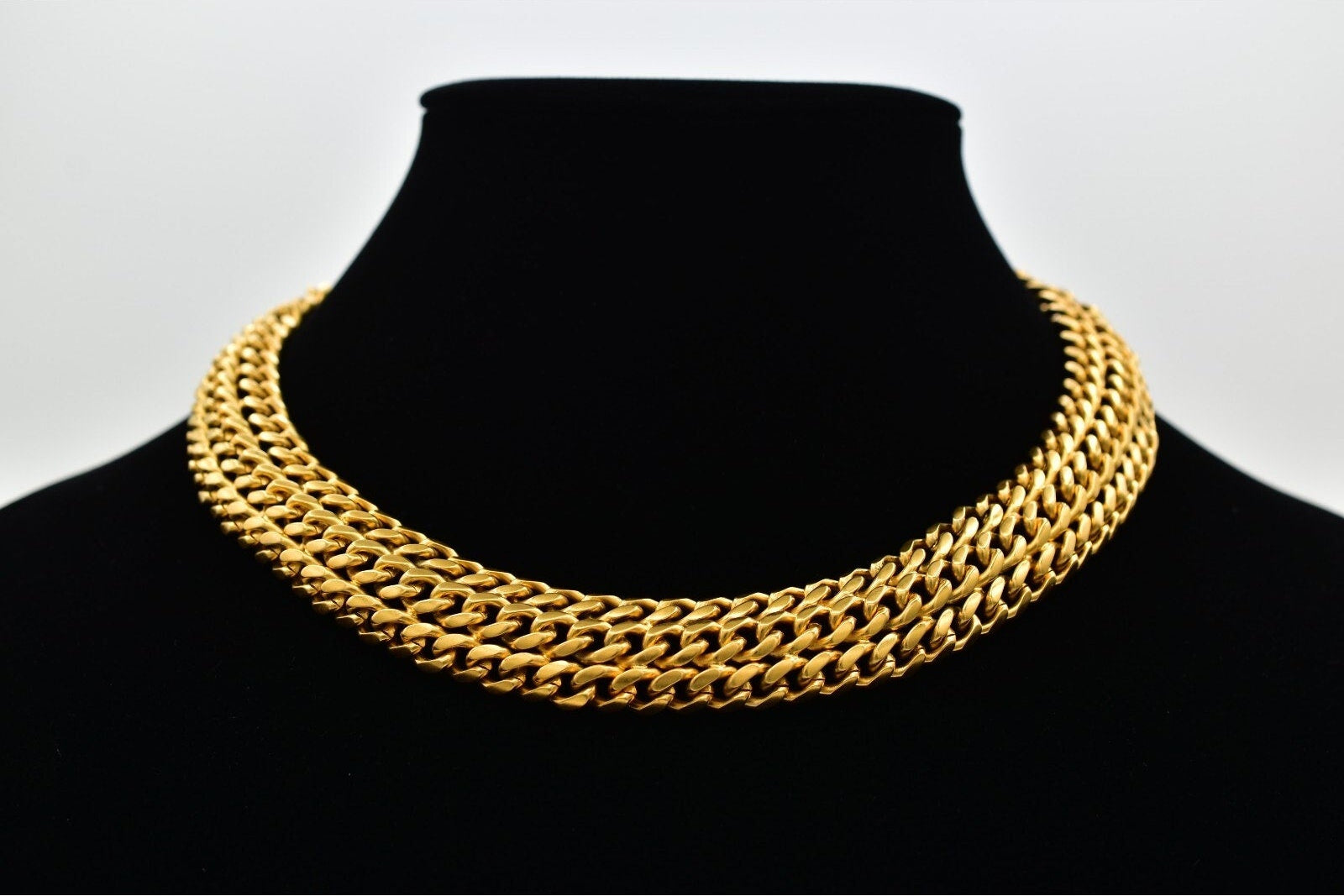 Gold chain necklace on a black mannequin against a white background