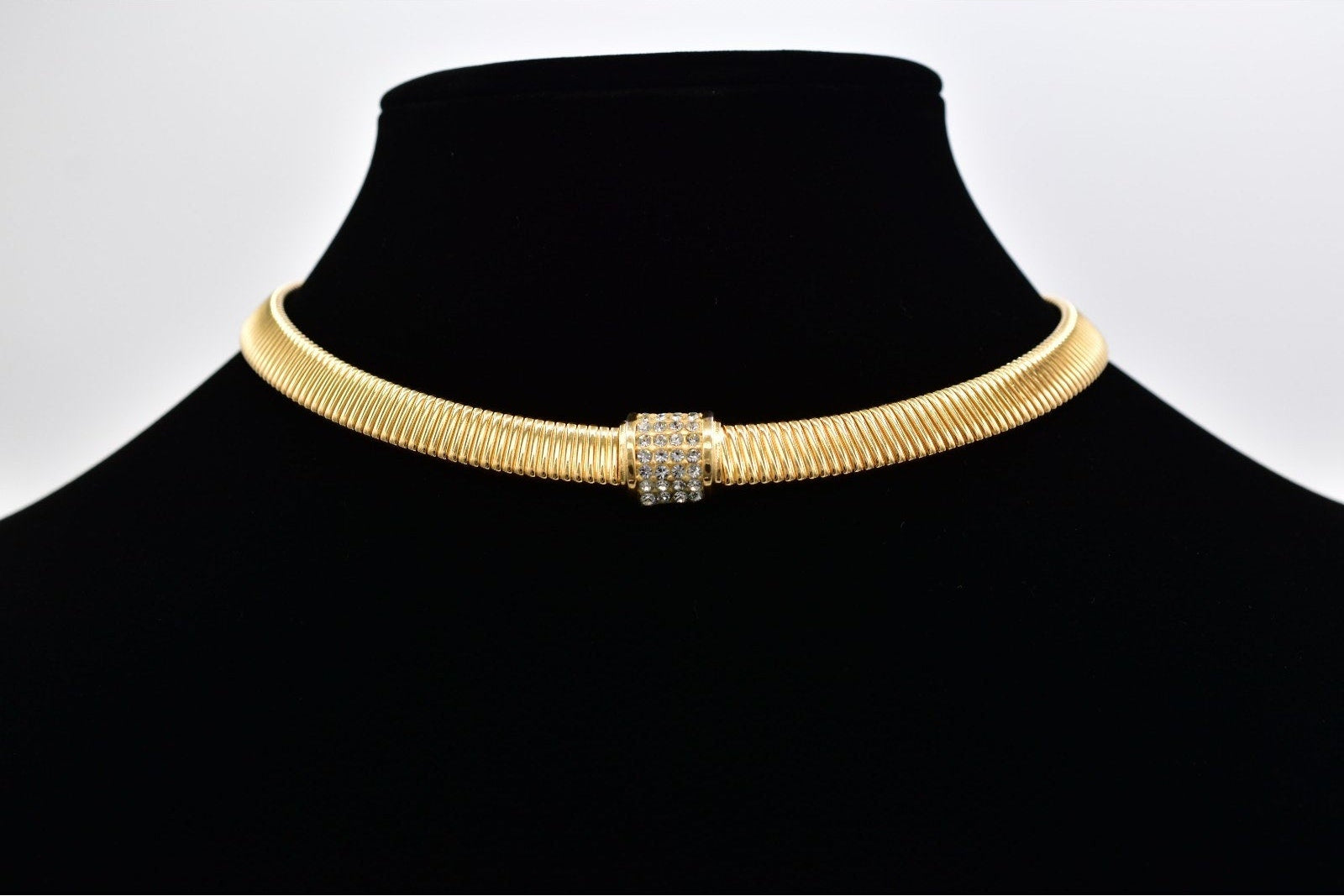 Gold choker necklace on a black mannequin with a white background