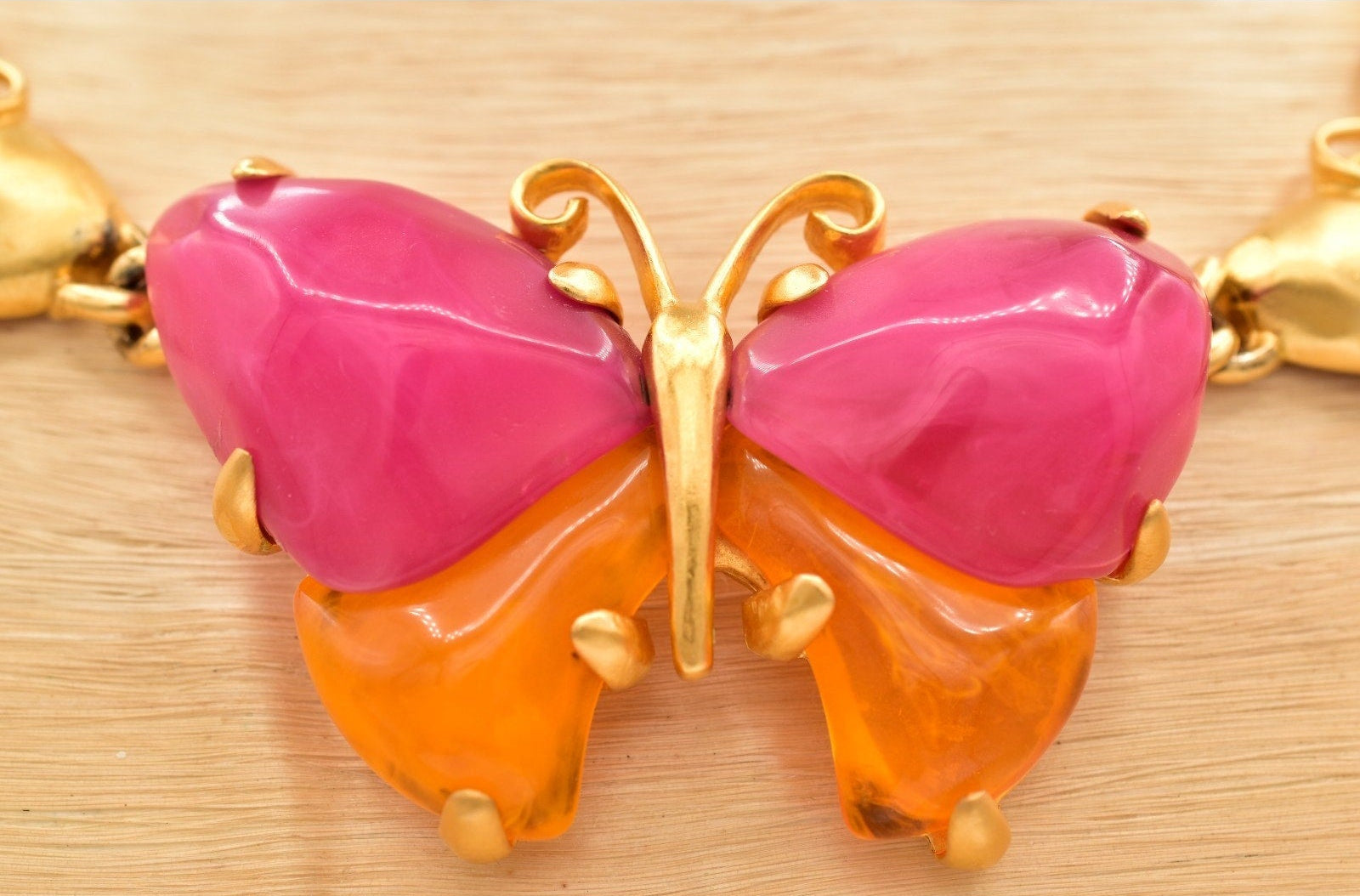 Close up of a vintage Givenchy gold butterfly necklace with pink and orange lucites on a black mannequin against a beige background.