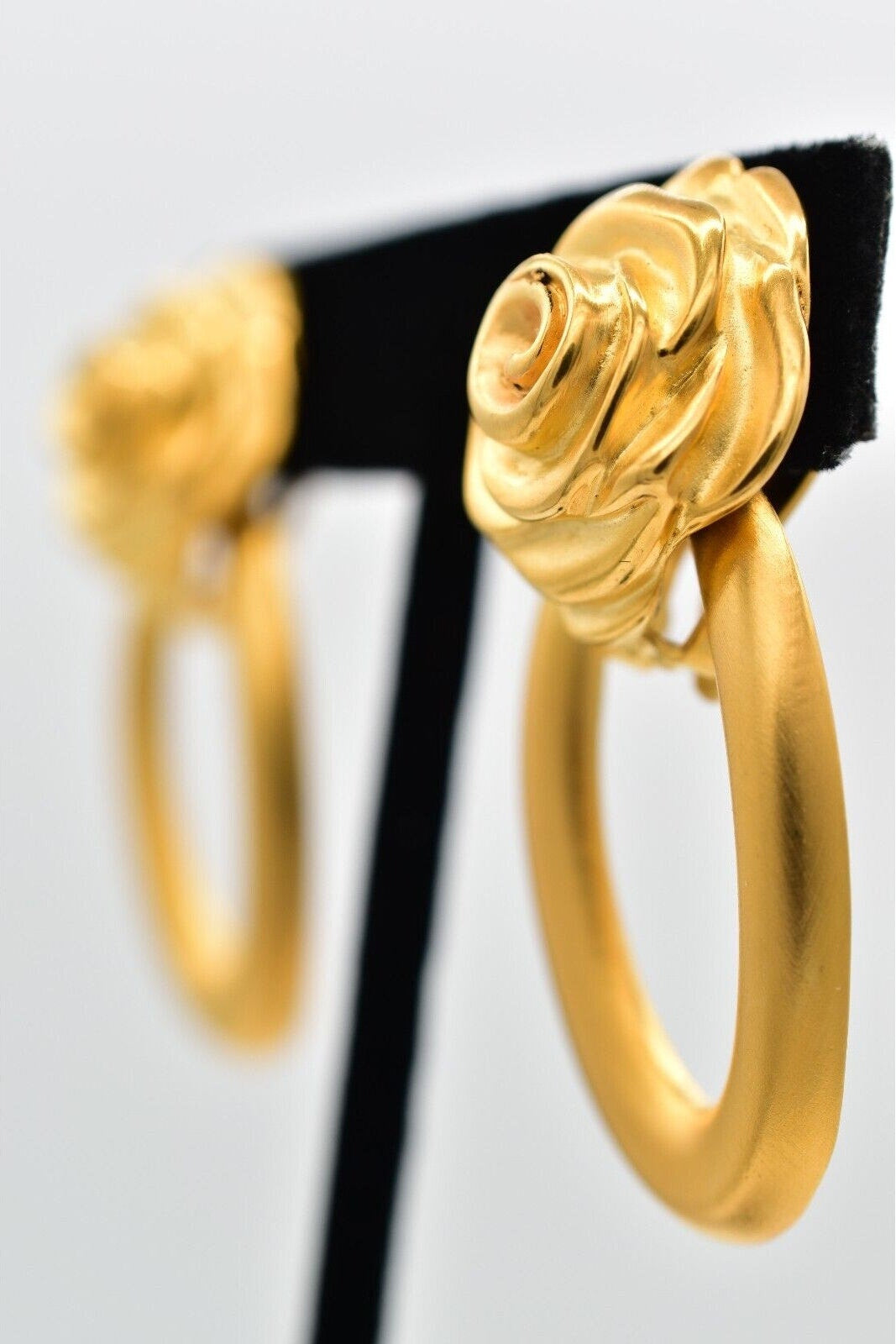 Gold hoop earrings on a black stand against a light gray background