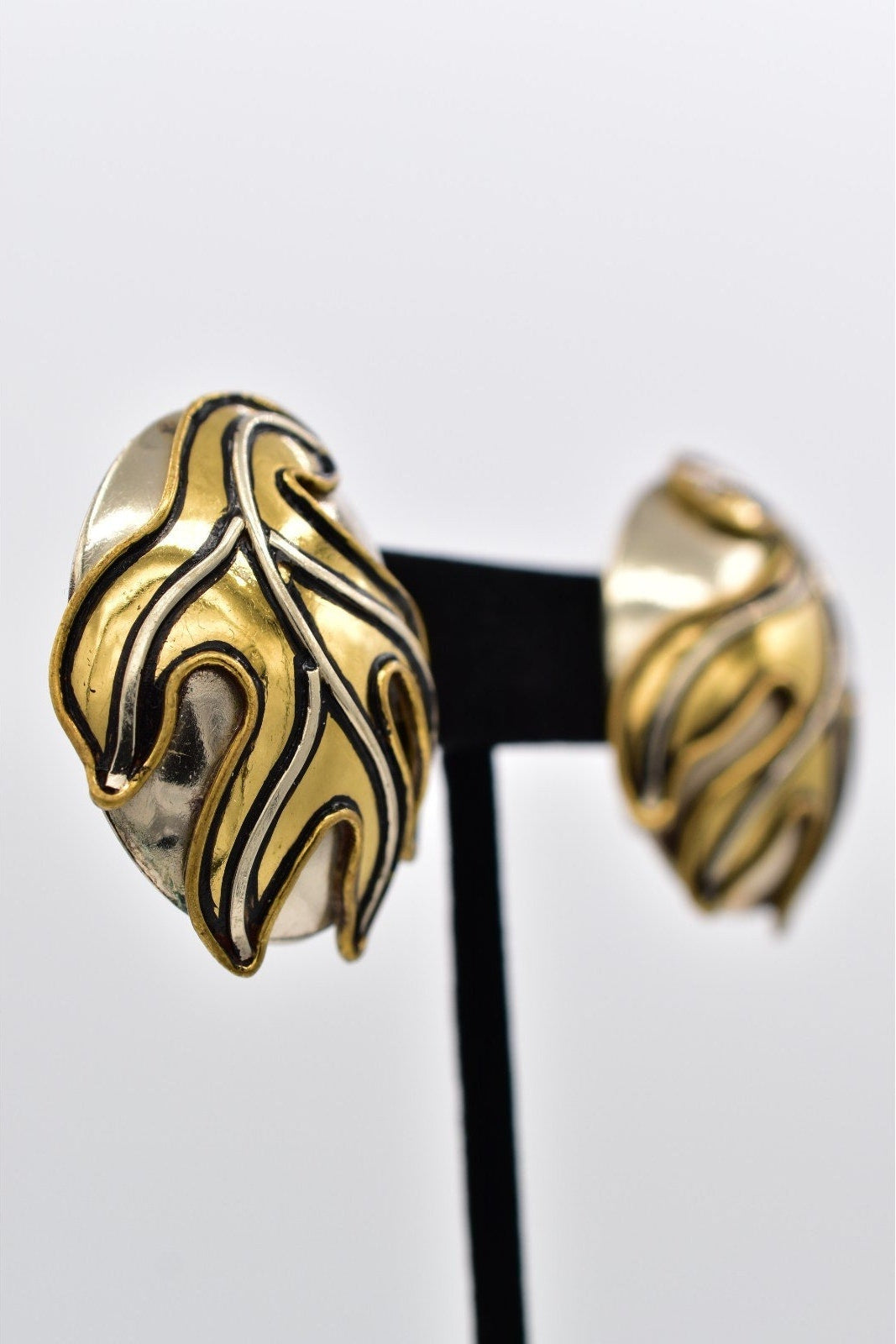 Gold and black feather-shaped earrings on a white background