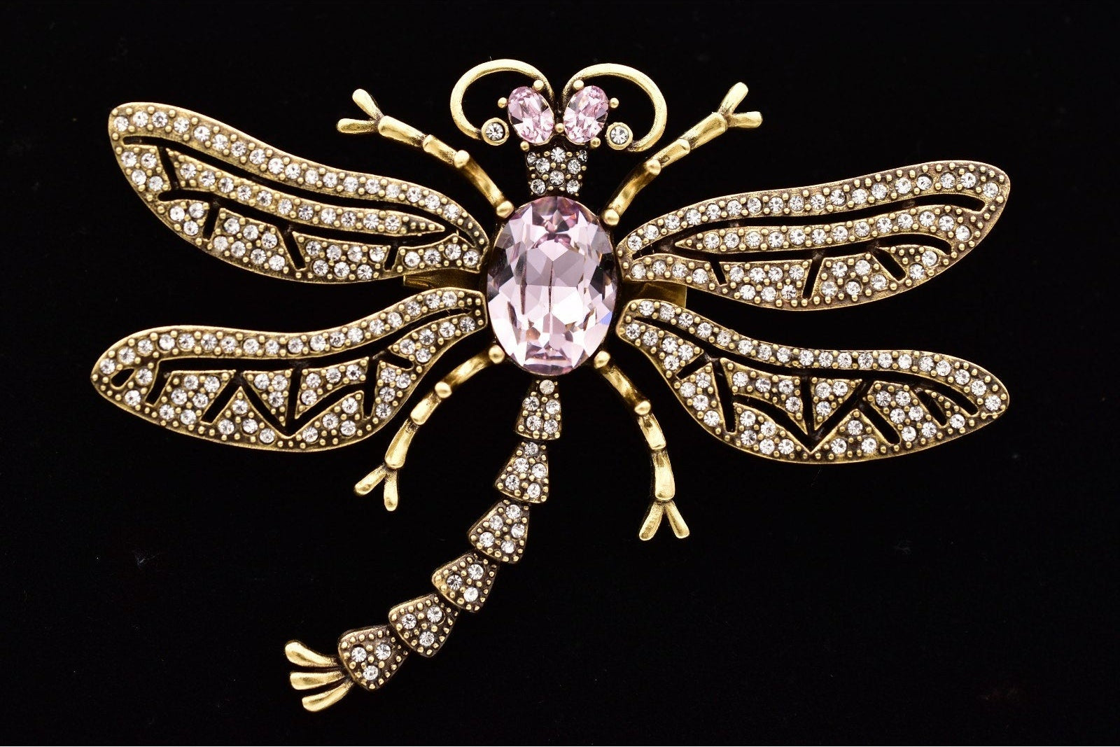 Gold dragonfly brooch with pink central gem on a black background