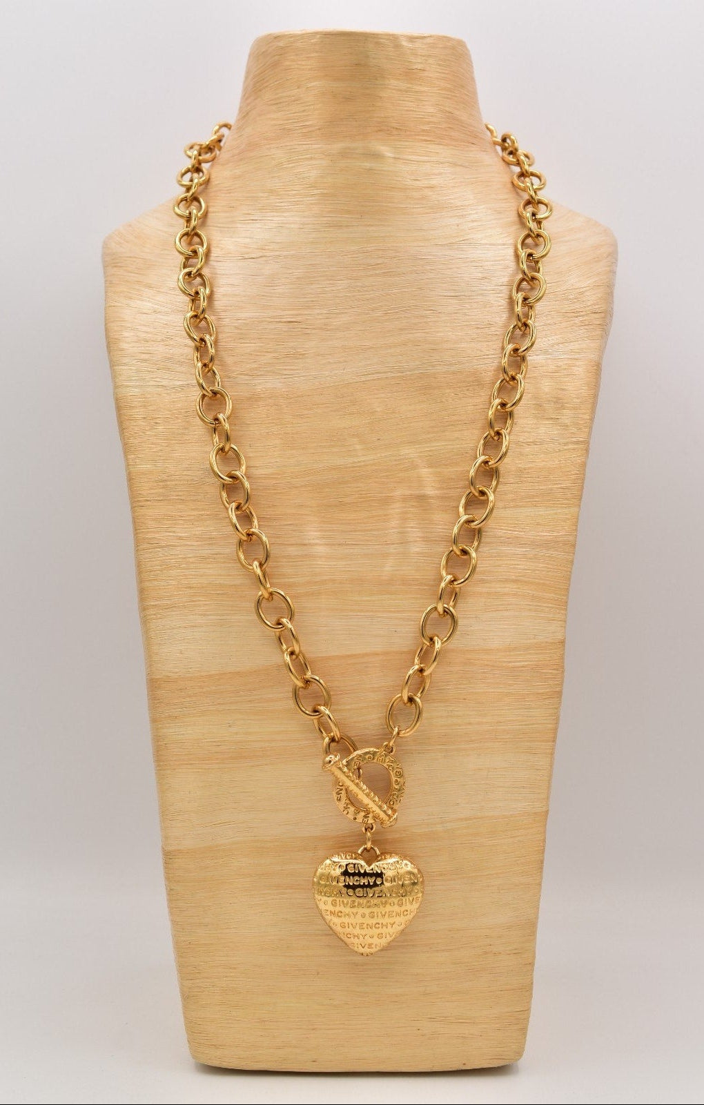 Gold chain necklace with heart-shaped pendant on a wooden mannequin bust.