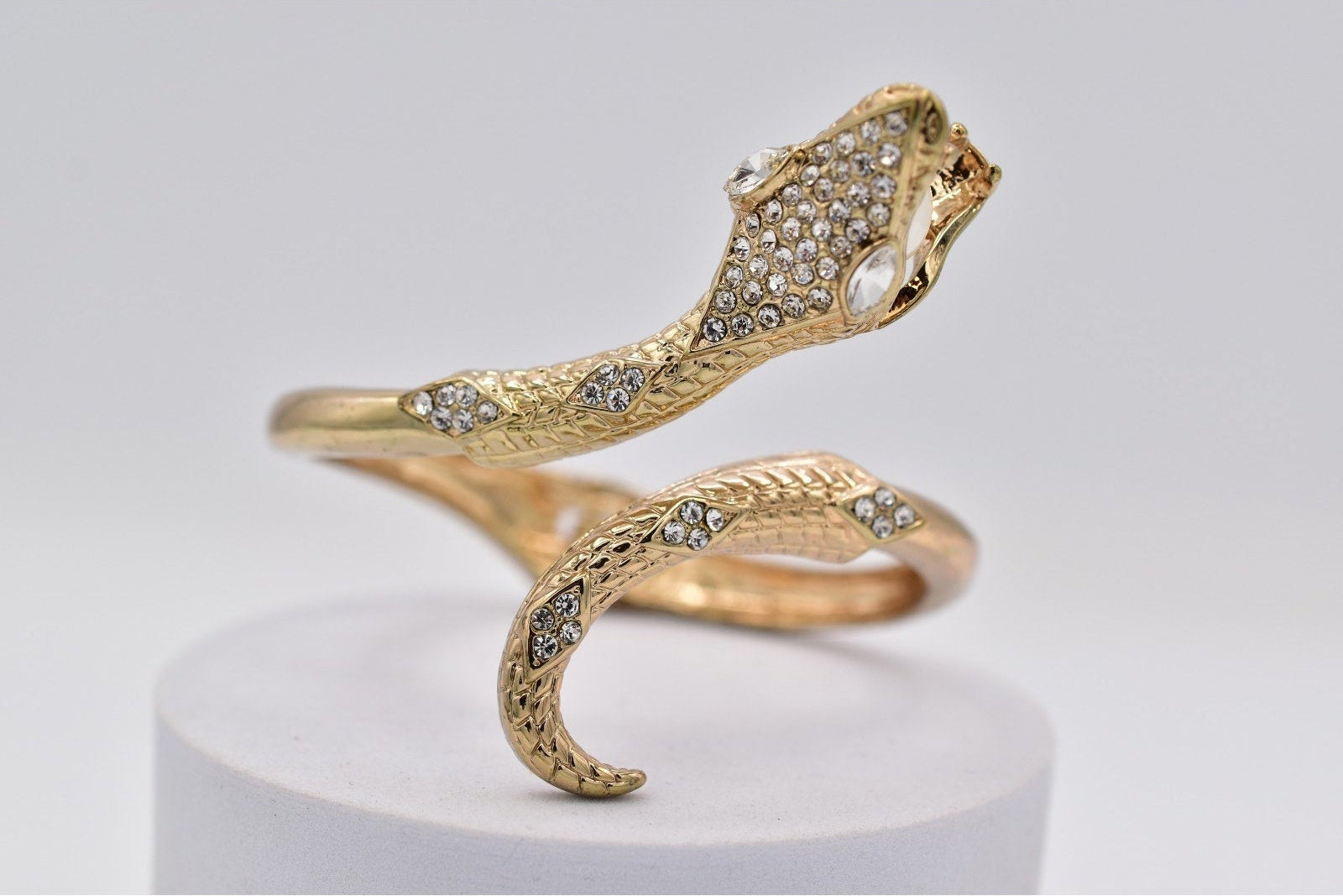 Gold snake-shaped ring with embedded stones on a light gray background