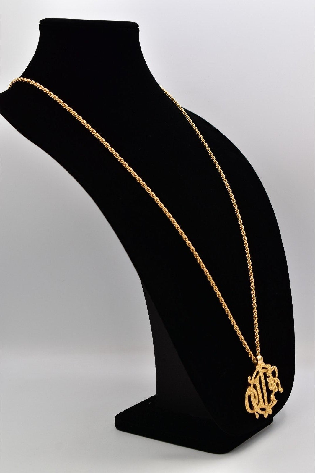 Gold necklace with a pendant on a black mannequin bust against a white background