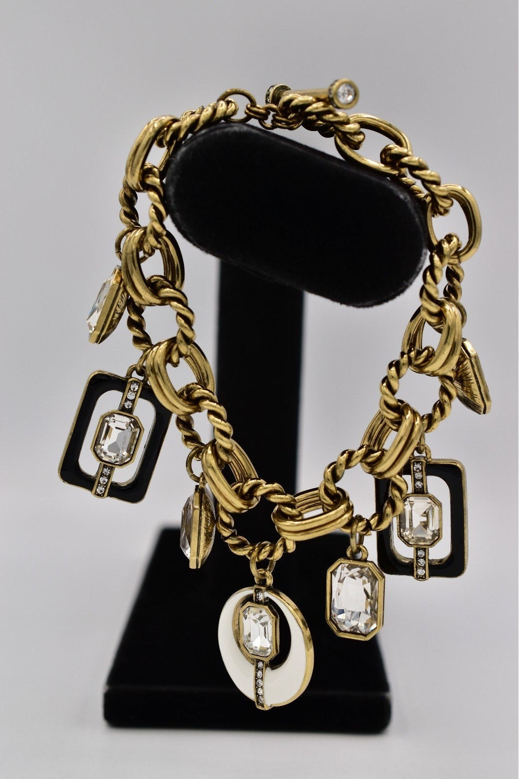 Gold chain bracelet with charms on a black stand against a gray background