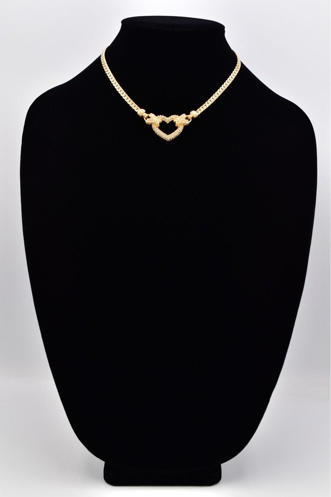 A gold heart-link chain necklace displayed on a black velvet jewelry bust against a light gray background.