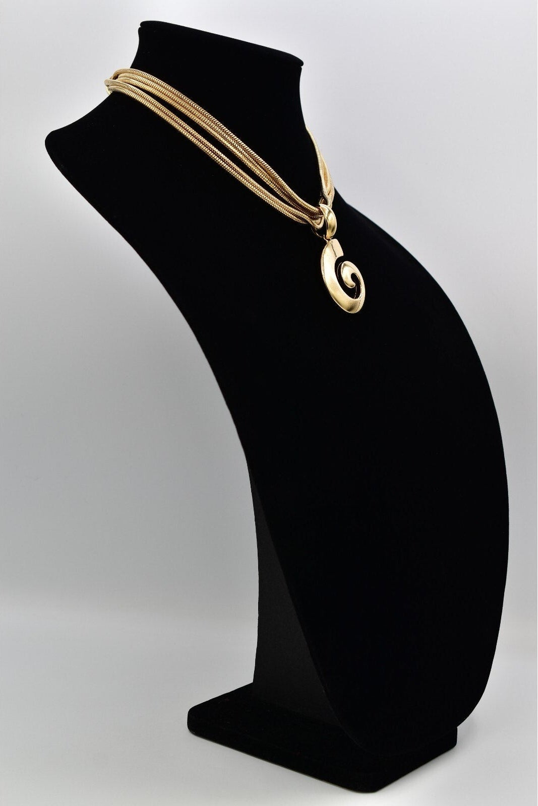 Gold necklace on a black bust against a white background