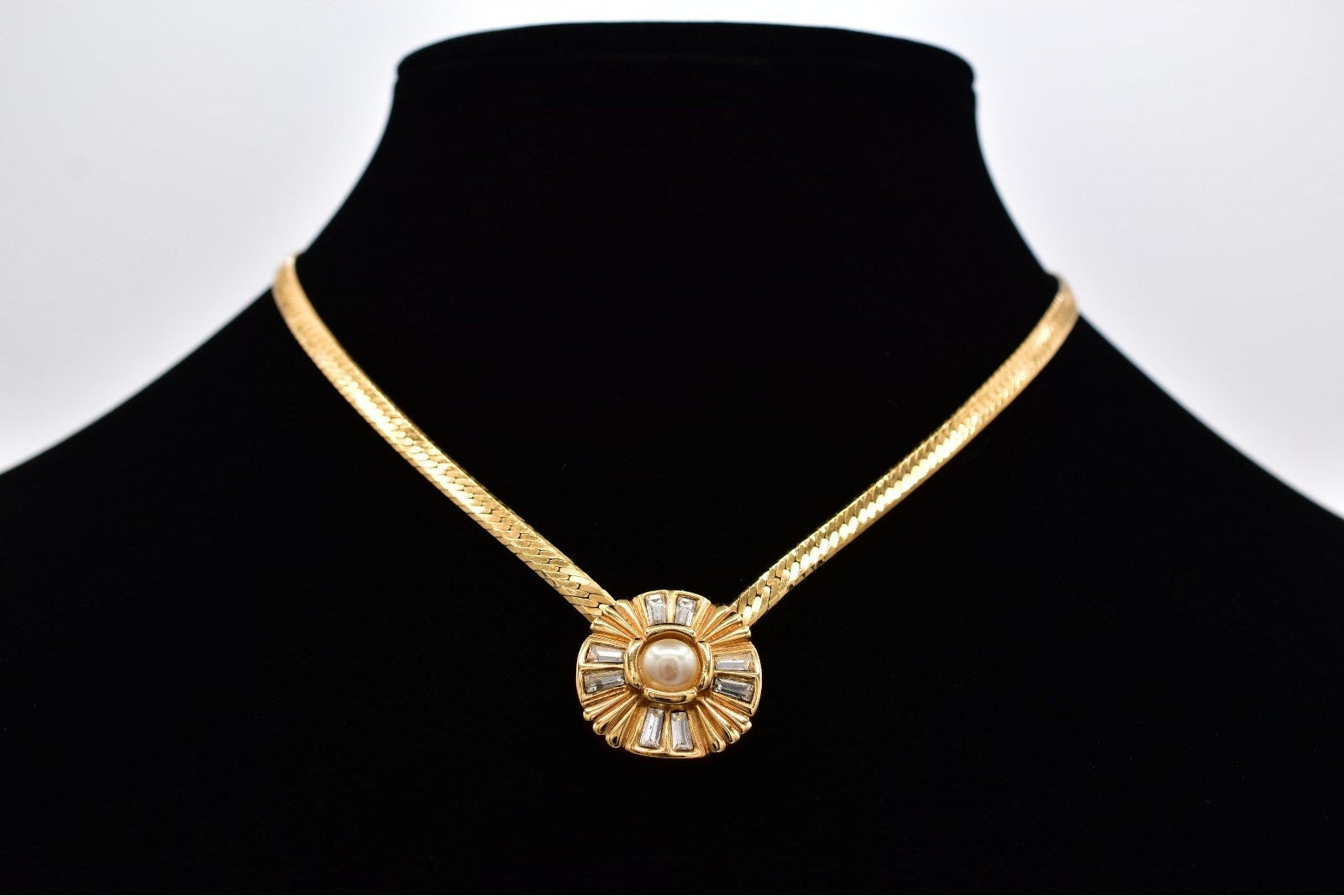 Gold necklace with a decorative pendant on a black mannequin against a white background