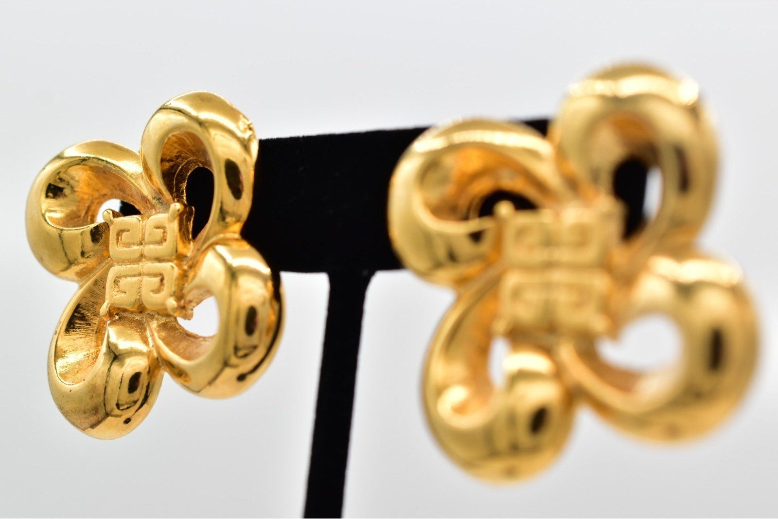 Pair of gold earrings on a black stand against a white background