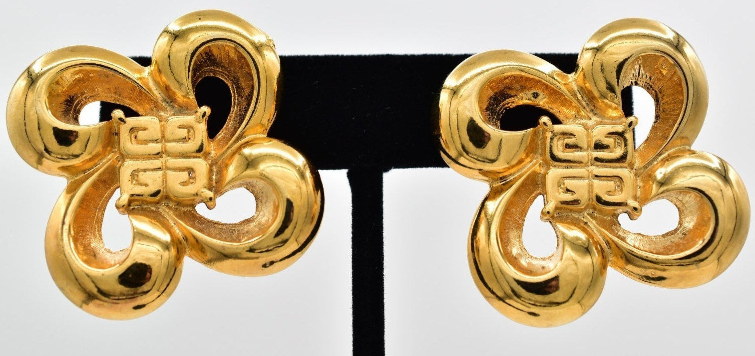 Pair of gold Givenchy earrings on a black stand against a white background