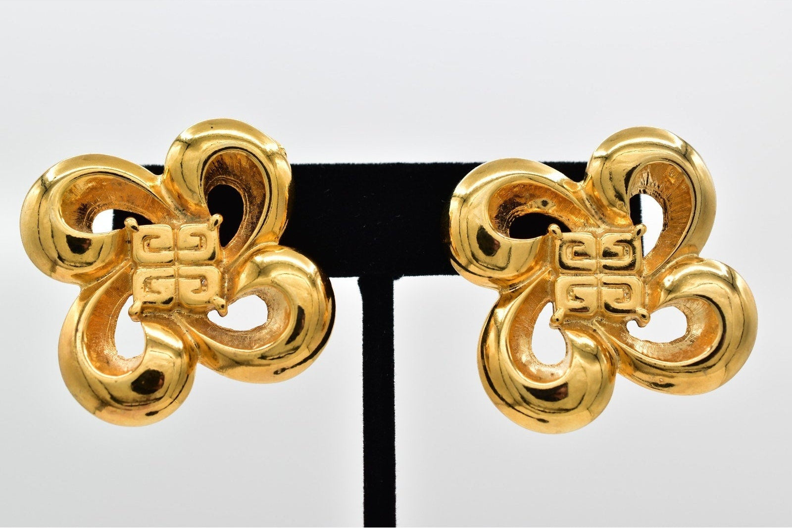 Pair of gold earrings on a black stand against a white background