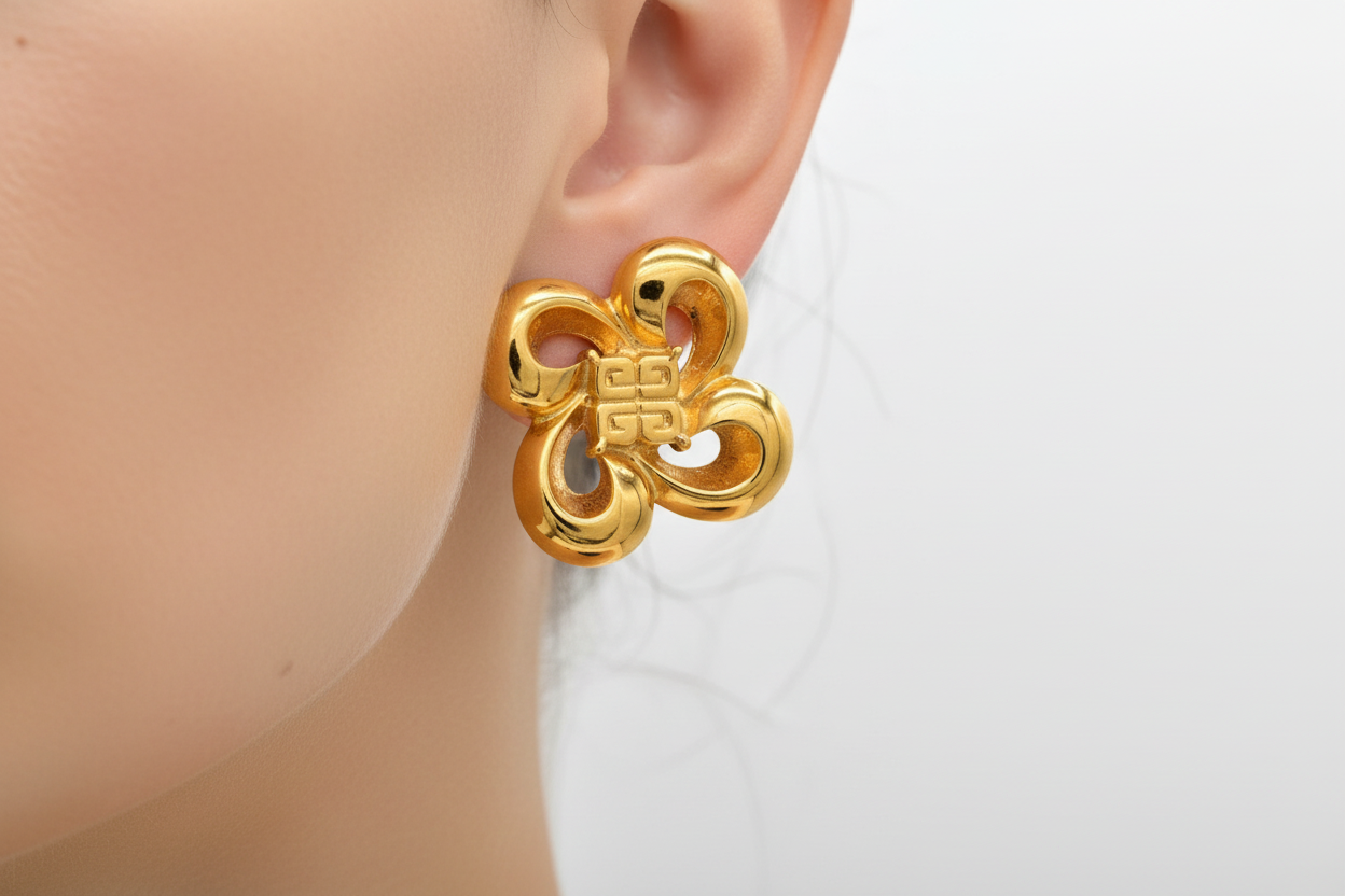 Pair of gold earrings on a black stand against a white background