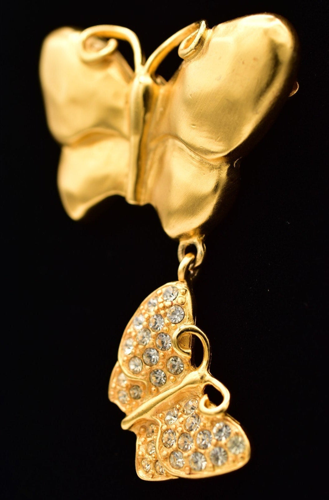 Gold butterfly-shaped earring with clear gemstones on a black background