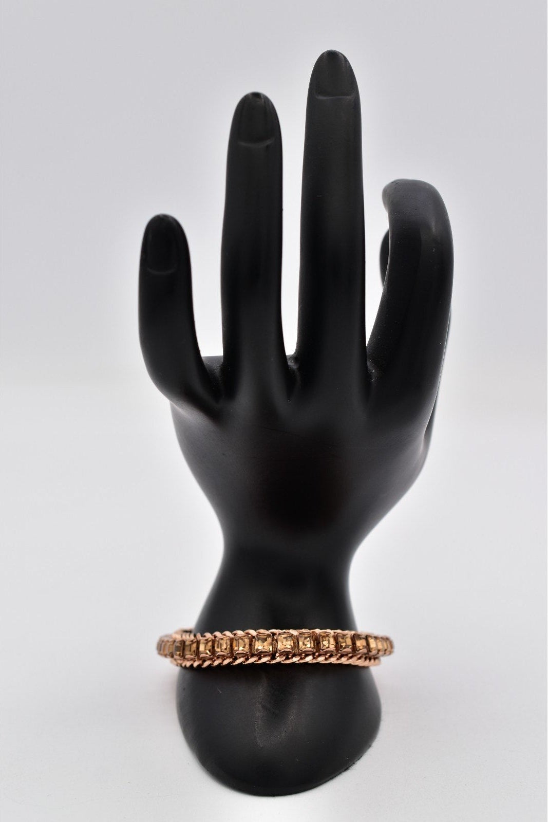 Black mannequin hand holding a gold bracelet on a white background