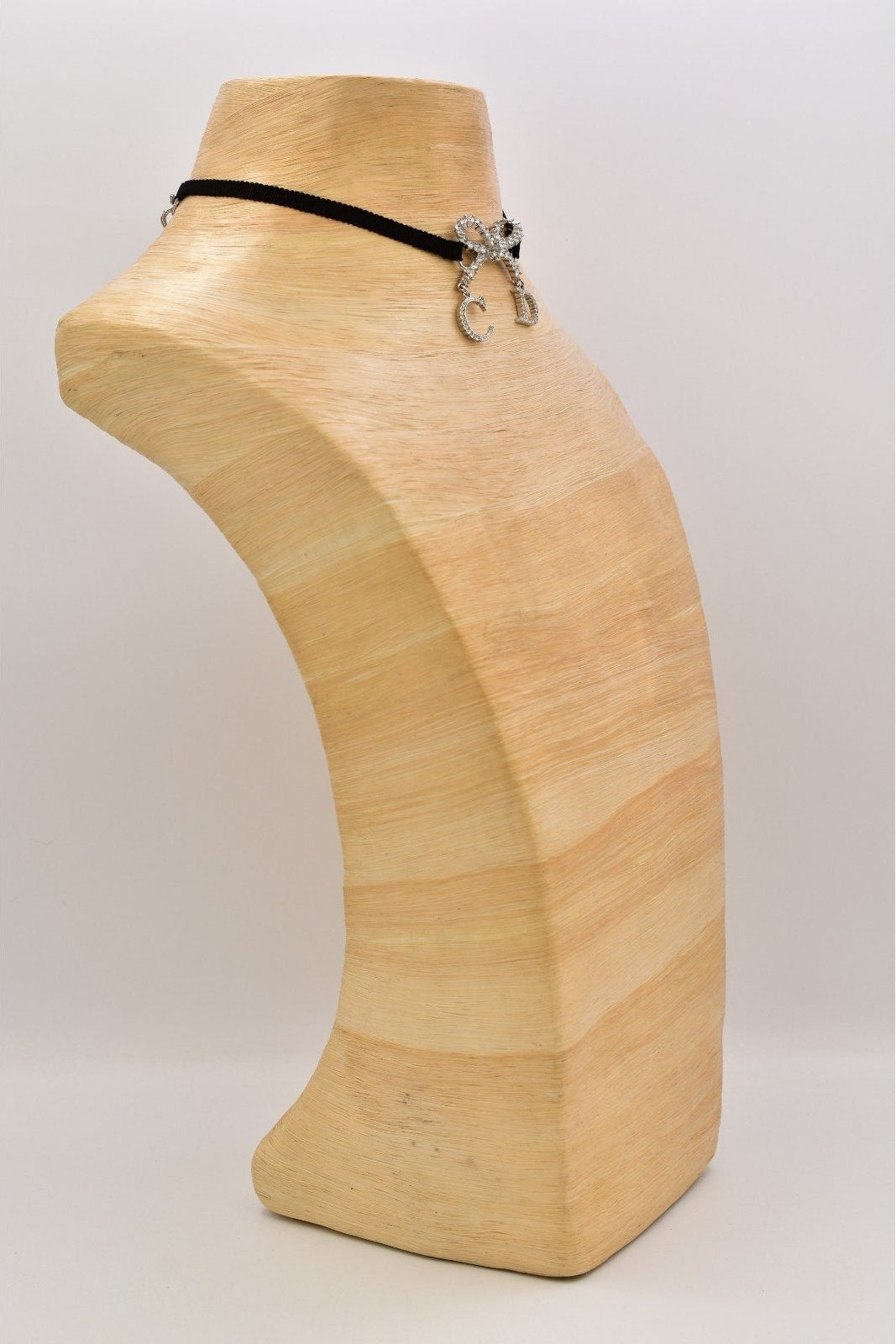 A black choker necklace with a silver-toned butterfly clasp, displayed on a light beige wooden mannequin bust against a neutral light gray background.