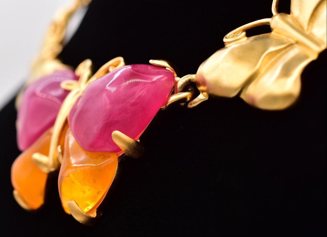 Close up of a vintage Givenchy gold butterfly necklace with pink and orange lucites on a black mannequin against a white background.