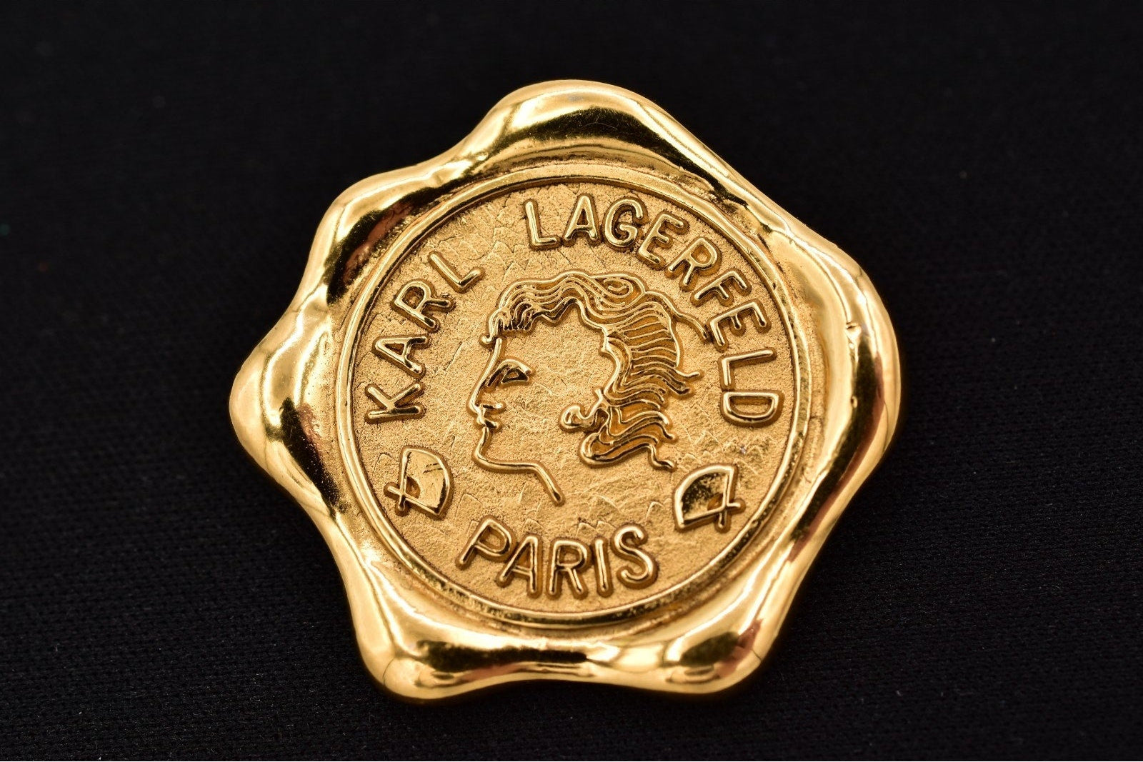 Gold wax seal stamp with Karl Lagerfeld's face and 'Karl Lagerfeld Paris' text on a black background
