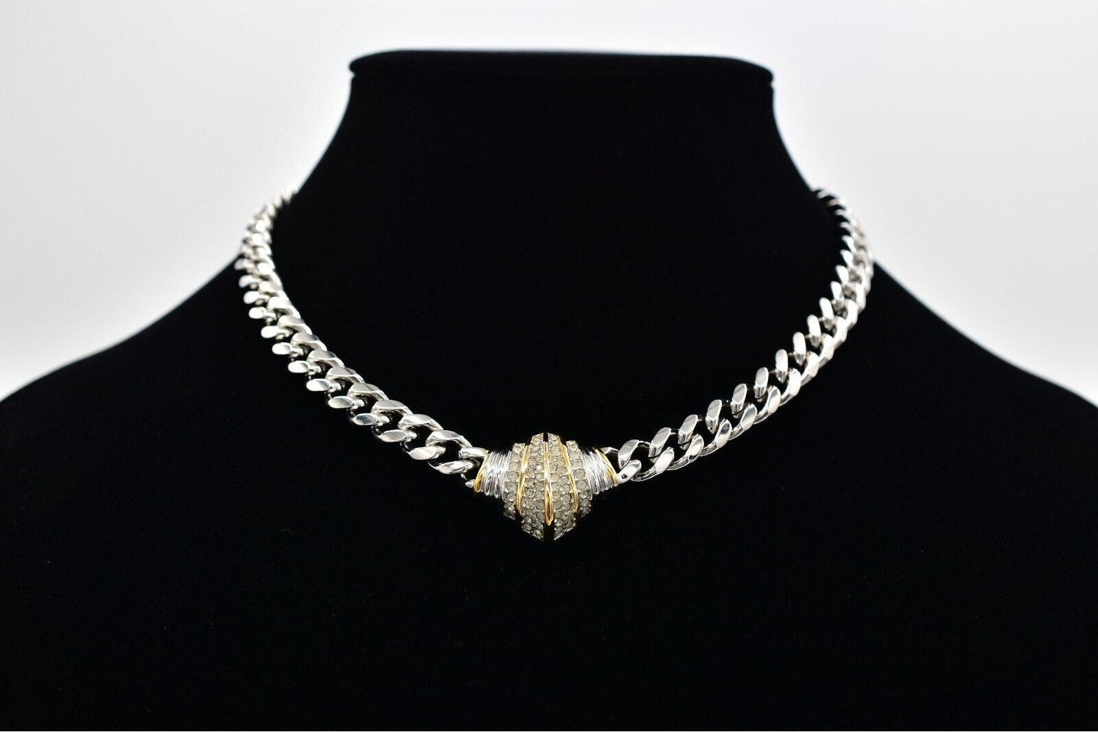 Silver chain necklace with a large decorative clasp on a black mannequin against a white background