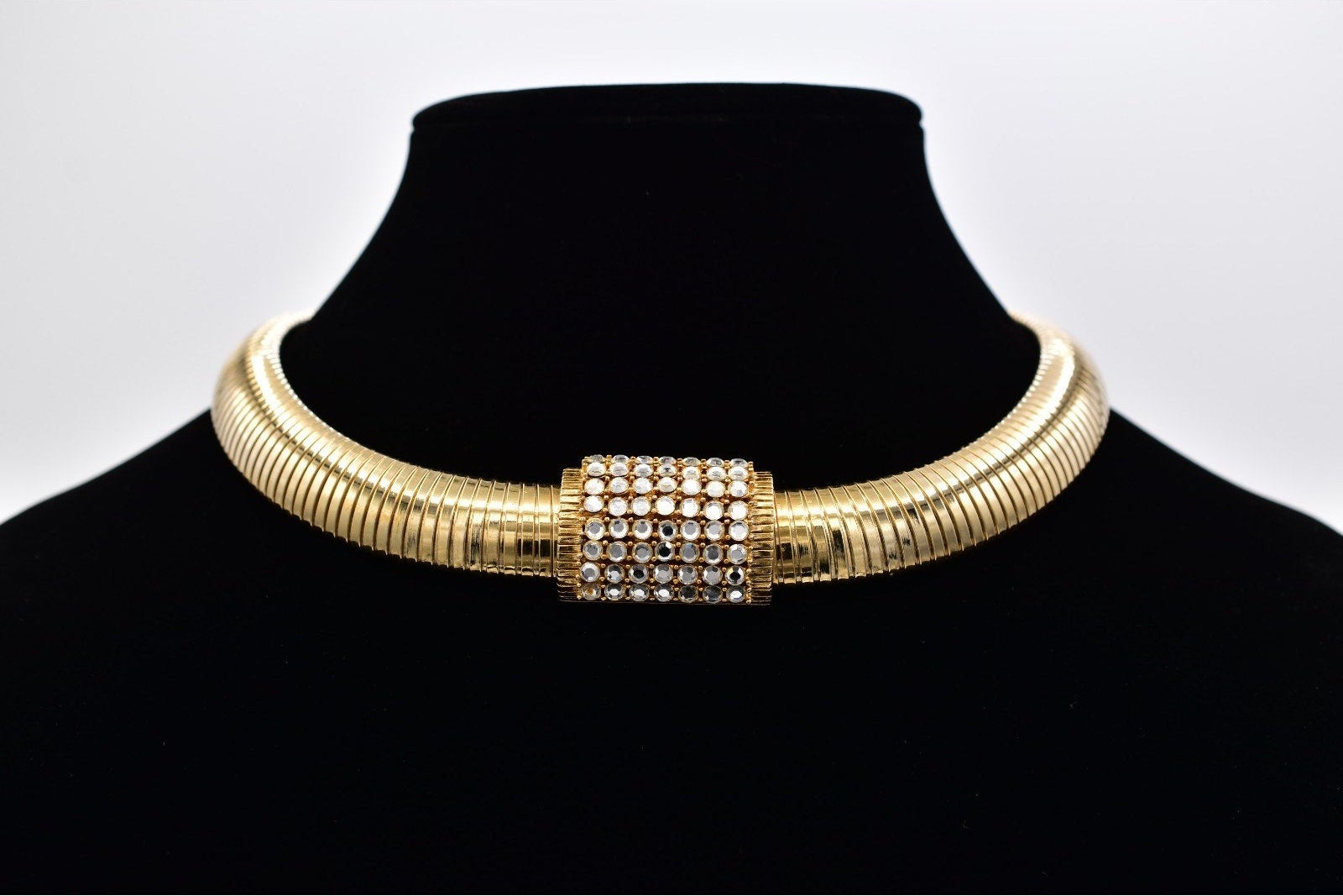 Gold choker necklace on a black mannequin bust with a white background