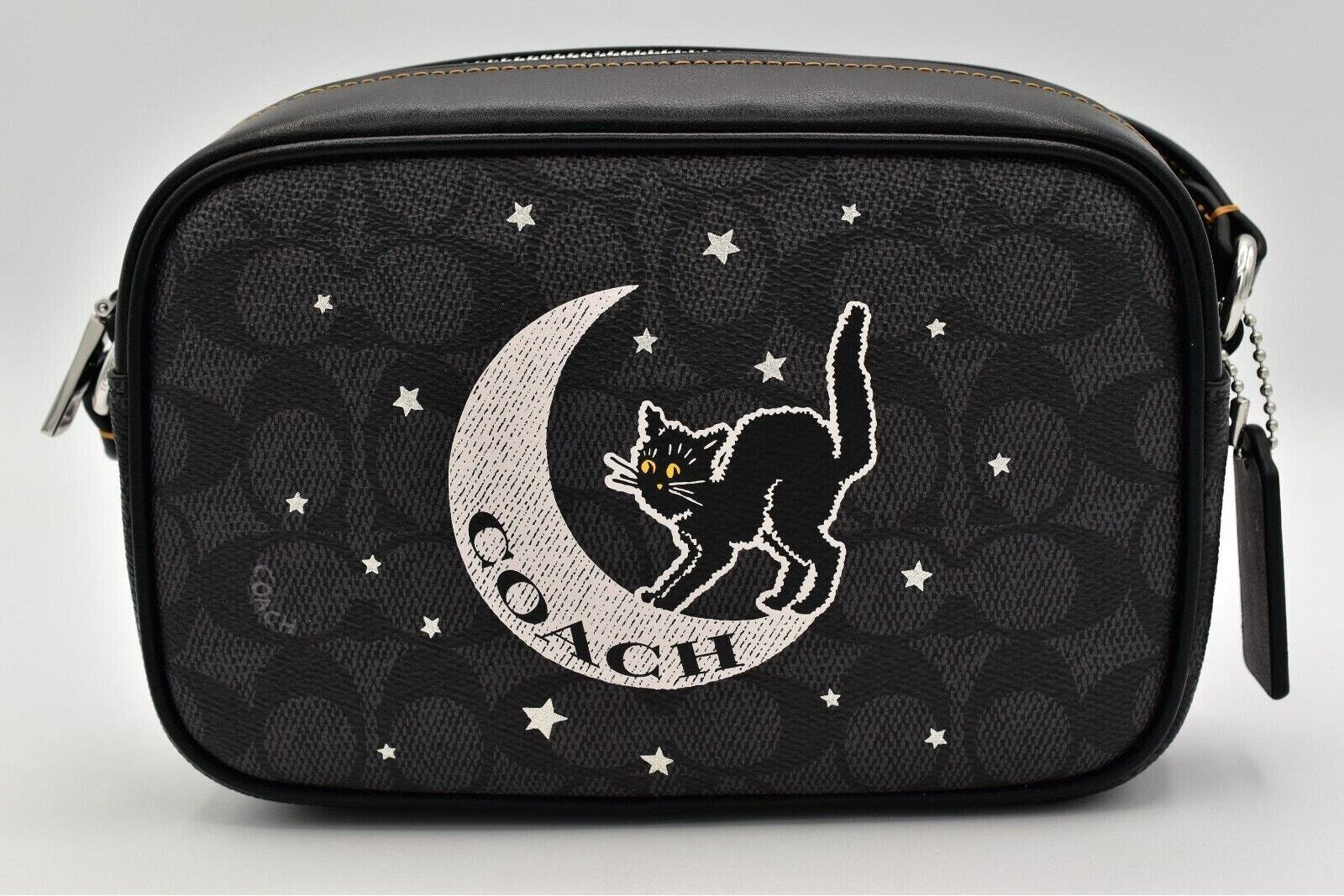 A Coach camera bag in black signature monogram canvas featuring a large embroidered black cat on a white crescent moon with the Coach logo, surrounded by white embroidered stars.
