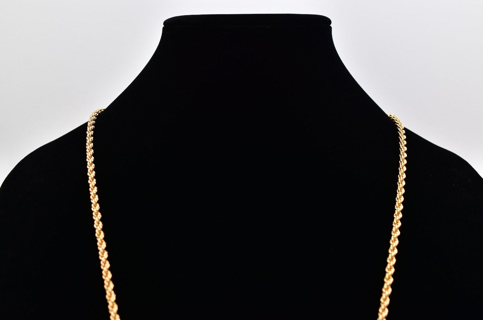 Gold chain necklace on a black mannequin against a white background