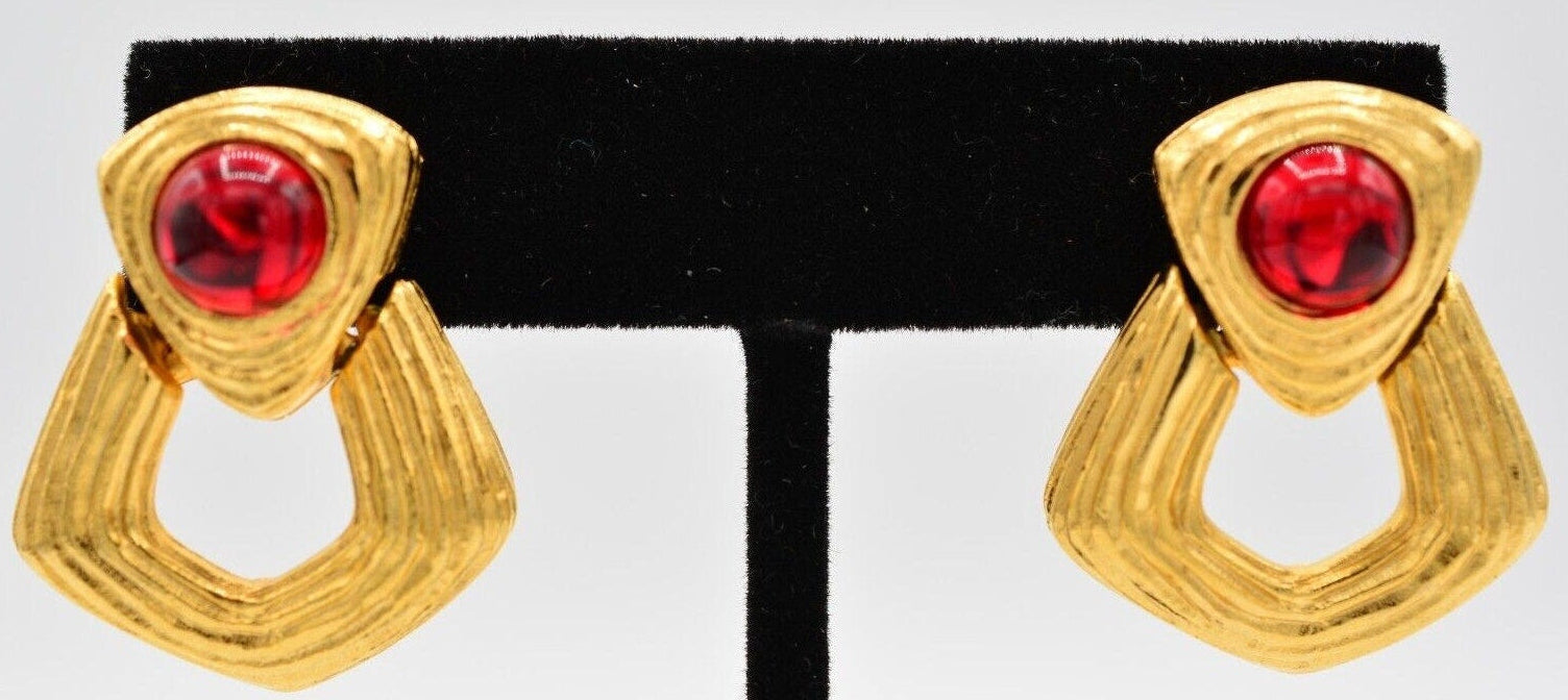 Gold earrings with red gemstones on a black and white earring stand.