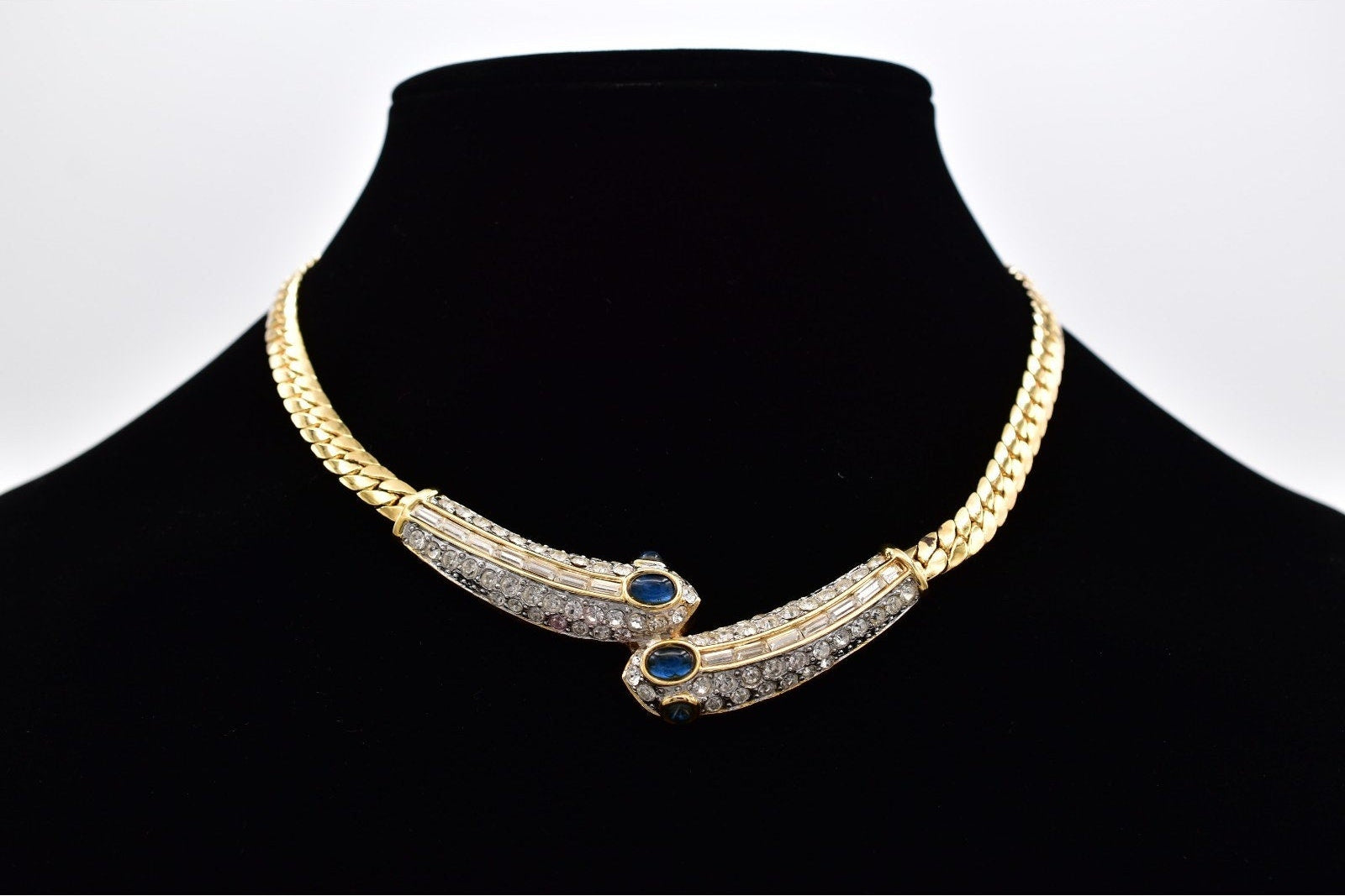 Gold and silver necklace with blue stones on a black mannequin against a white background