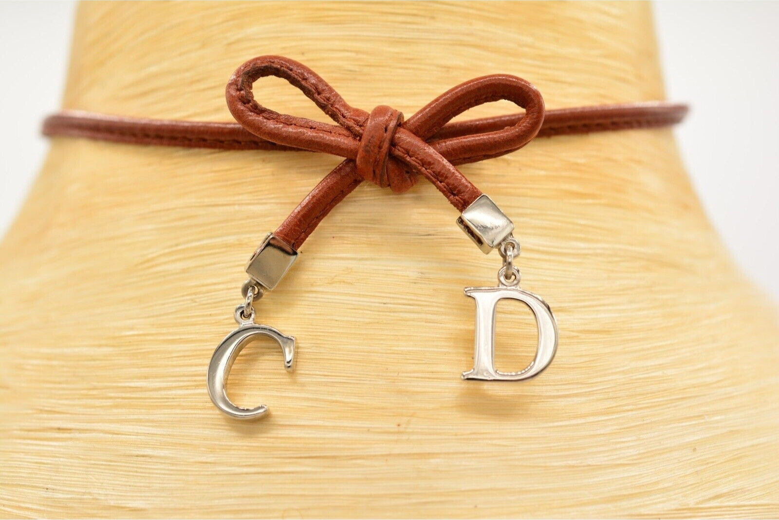 View of the front of a vintage brown leather Christian Dior choker necklace with a bow tied in the middle and dangling silver CD charms