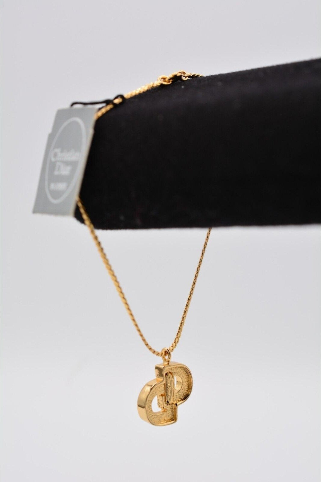  View of the back of a vintage gold Christian Dior rhinestone encrusted CD charm bracelet on a black velvet stand with the manufacturer's hang tag and the maker's mark visible