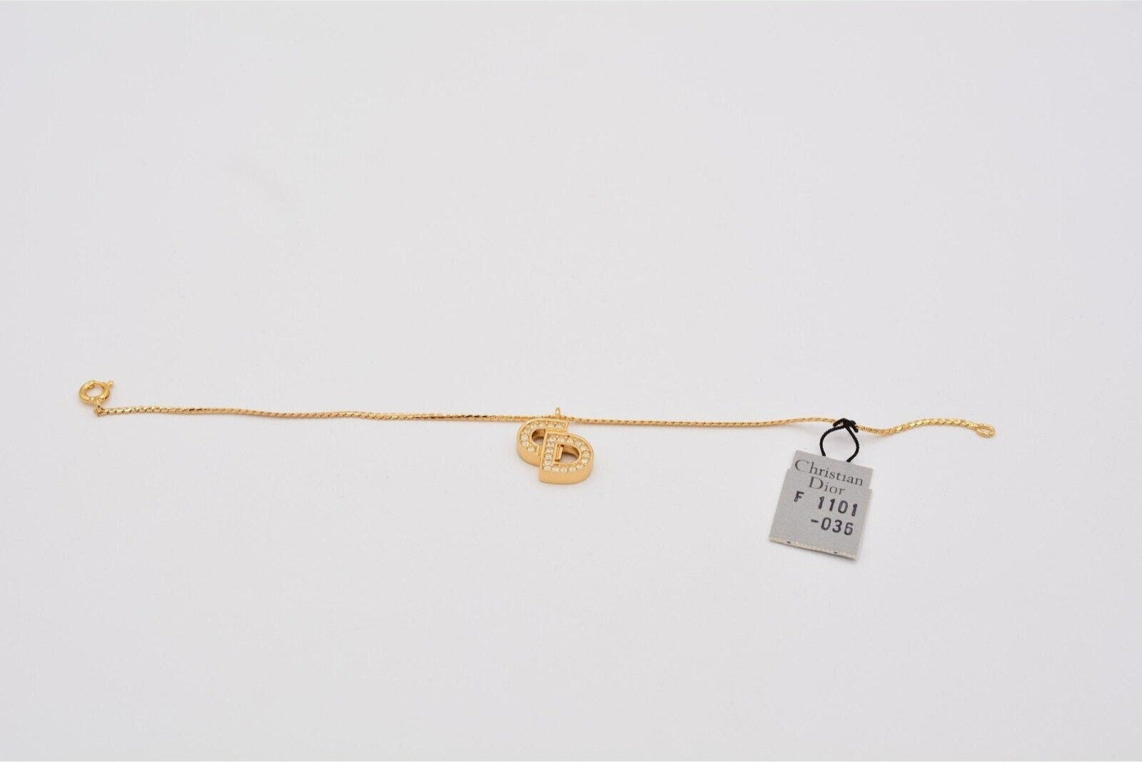 Vintage gold Christian Dior rhinestone encrusted CD charm bracelet laying flat with the hang tag showing