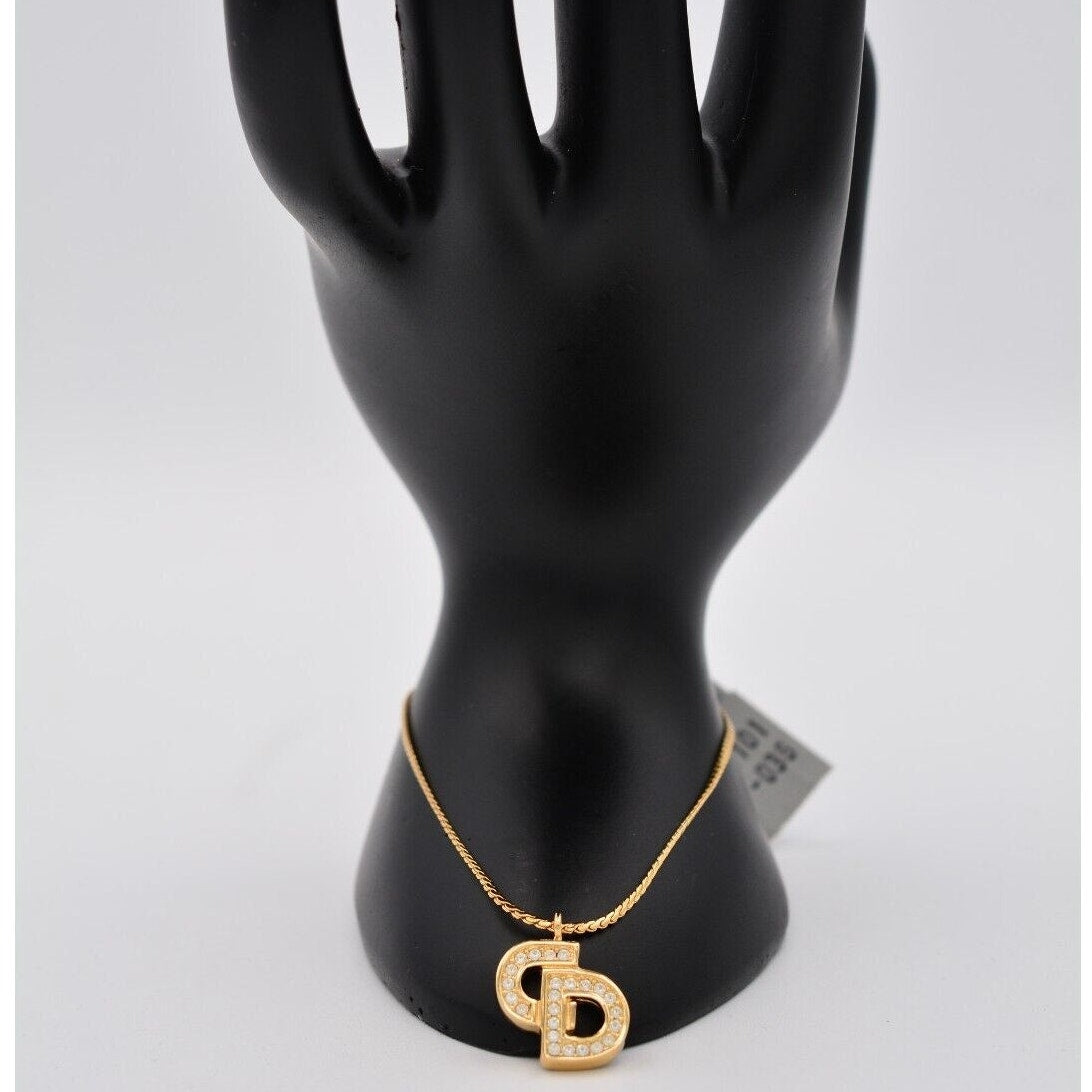 Top view of a vintage gold Christian Dior rhinestone encrusted CD charm bracelet on a black mannequin hand