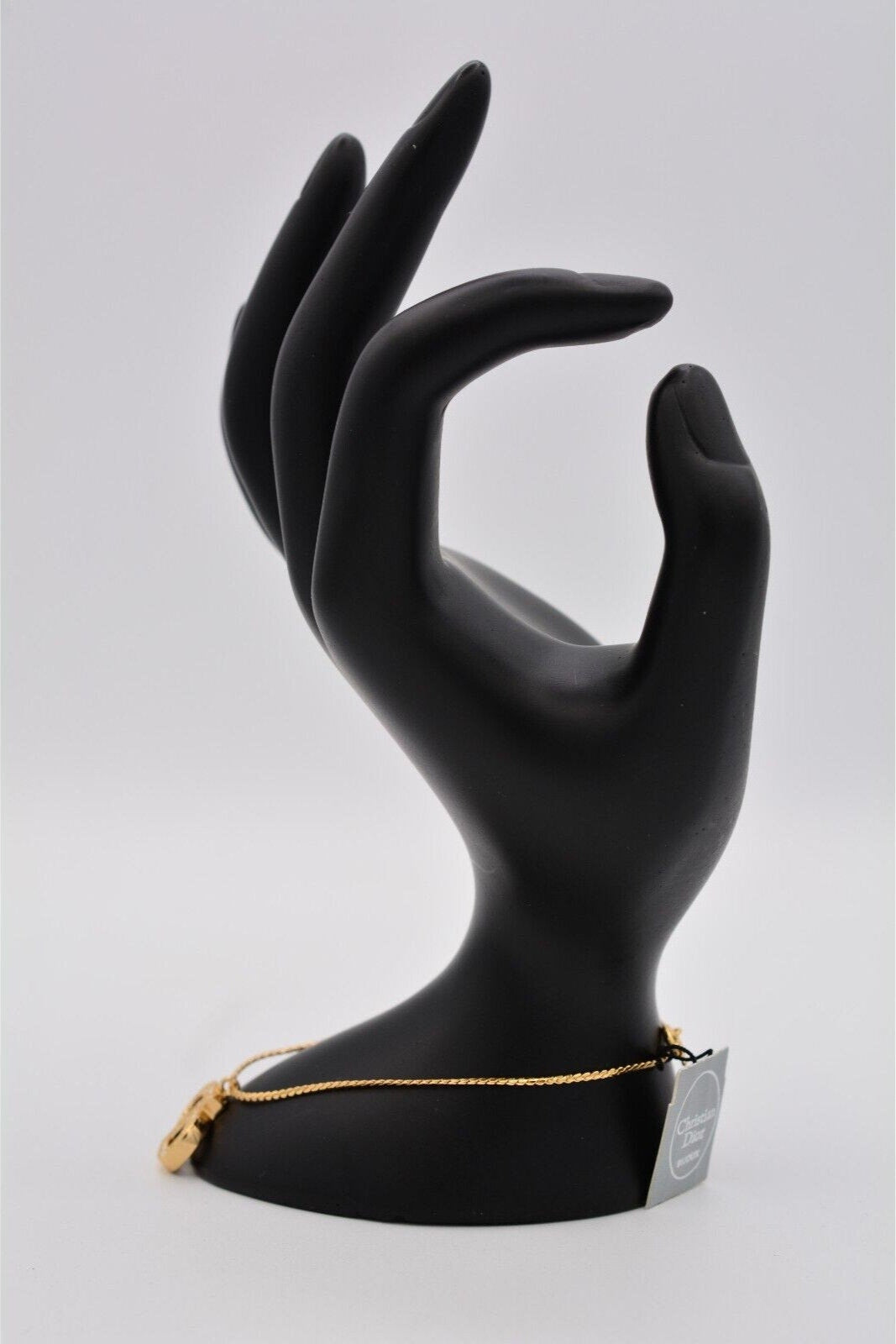 Side view of a vintage gold Christian Dior rhinestone encrusted CD charm bracelet on a black mannequin hand