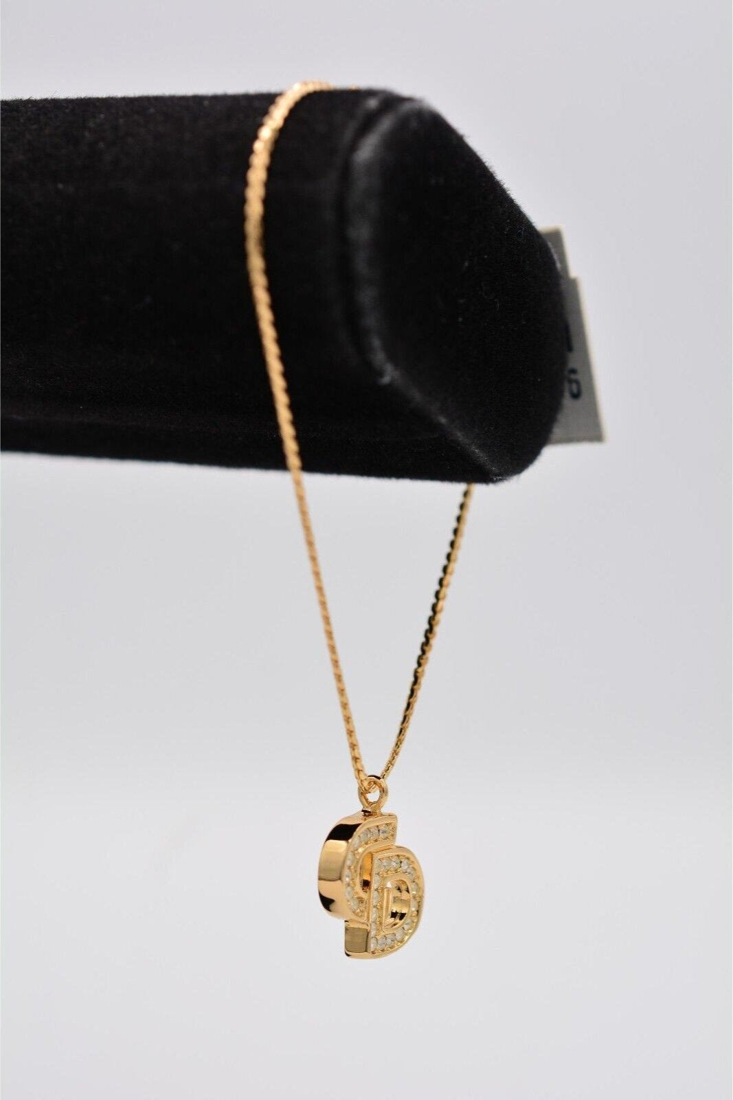 Side view of a vintage gold Christian Dior rhinestone encrusted CD charm bracelet on a black velvet stand 