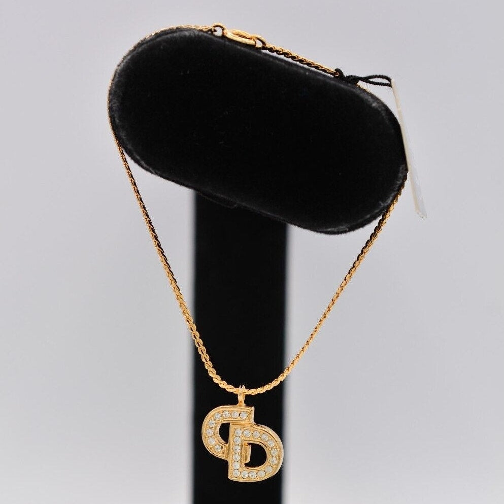 Side view of a vintage gold Christian Dior rhinestone encrusted CD charm bracelet on a black velvet stand 