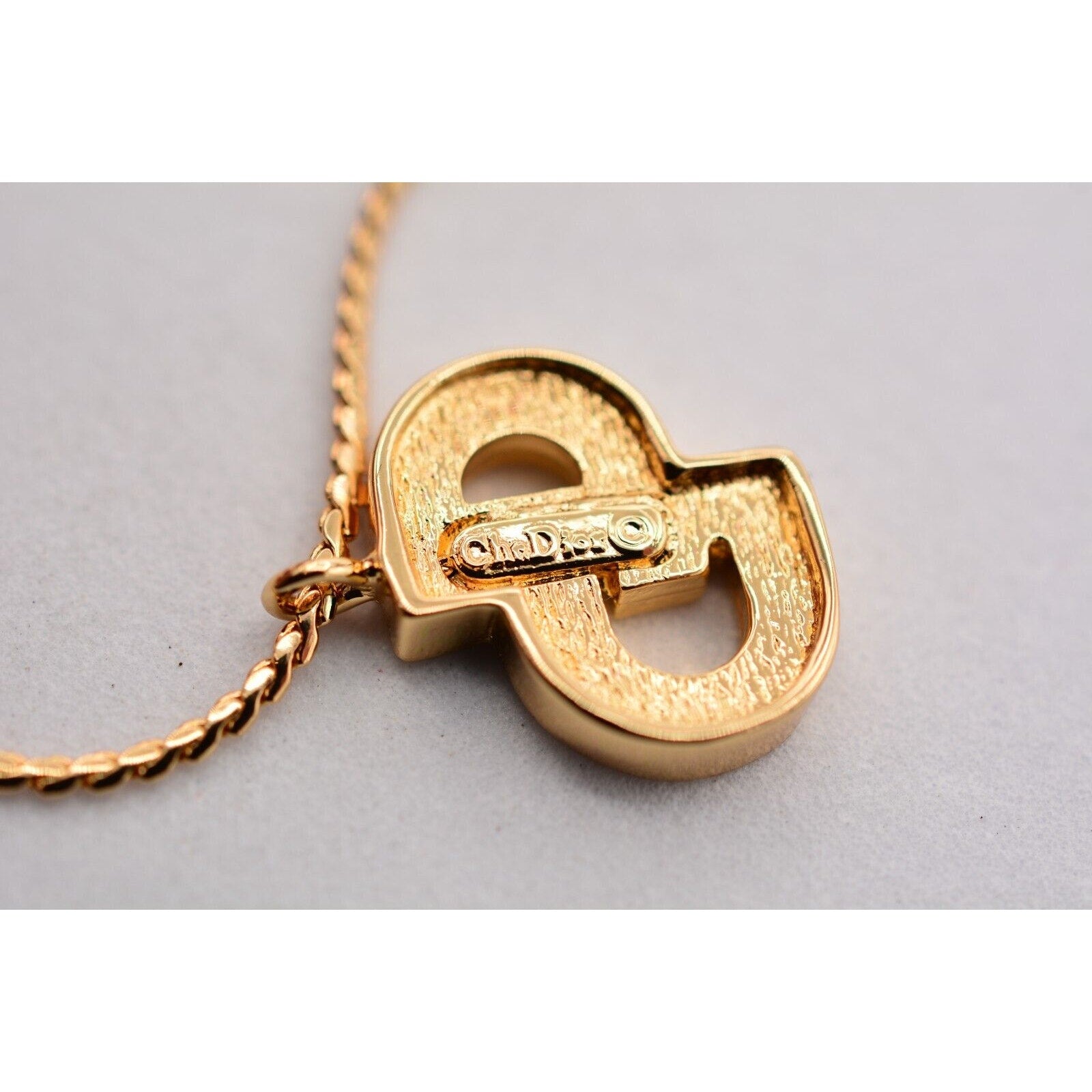 Close up view of a the manufacturer's signature on the back of a vintage gold Christian Dior rhinestone encrusted CD charm bracelet