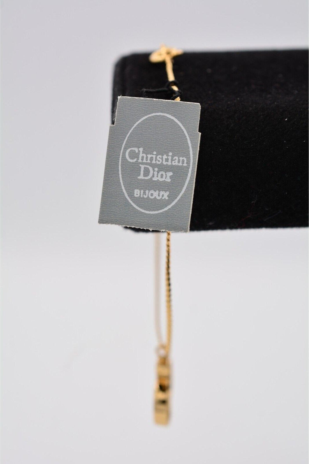 View of the vintage Christian Dior manufacturer's tag on a vintage gold Christian Dior rhinestone encrusted CD charm bracelet on a black velvet stand 