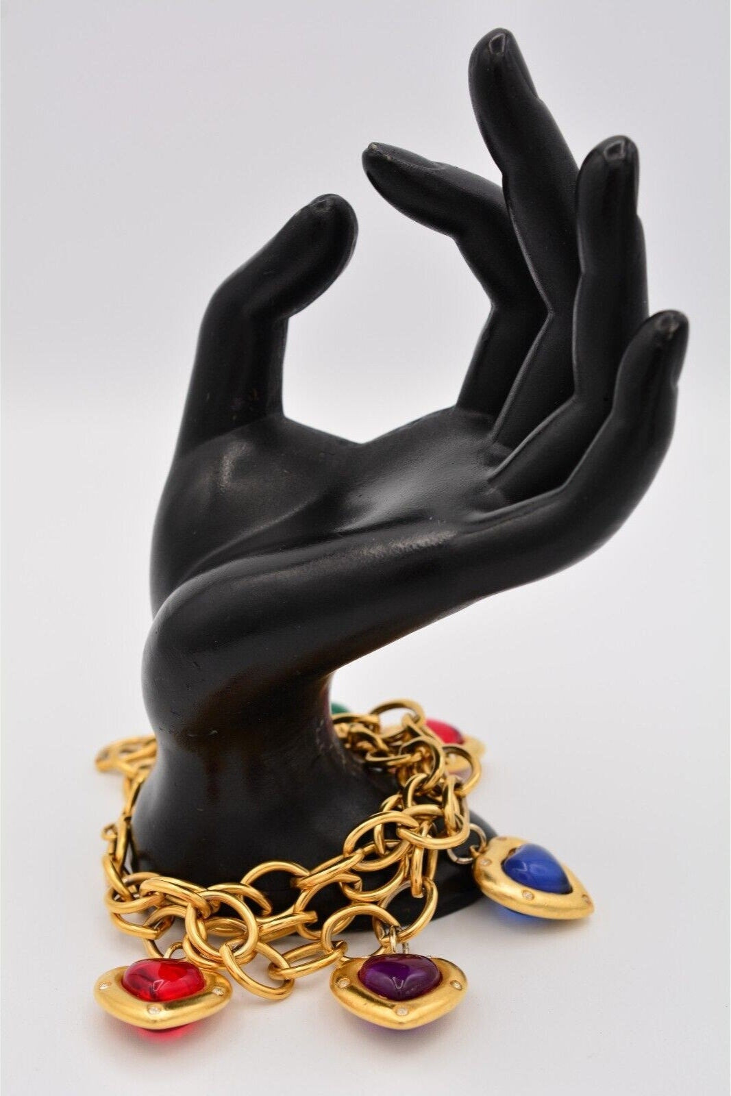Gold charm bracelet with multiple heart-shaped pendants in red, green, purple, and blue, featuring a glossy, puffy design and small embedded crystals, with gold chain links.