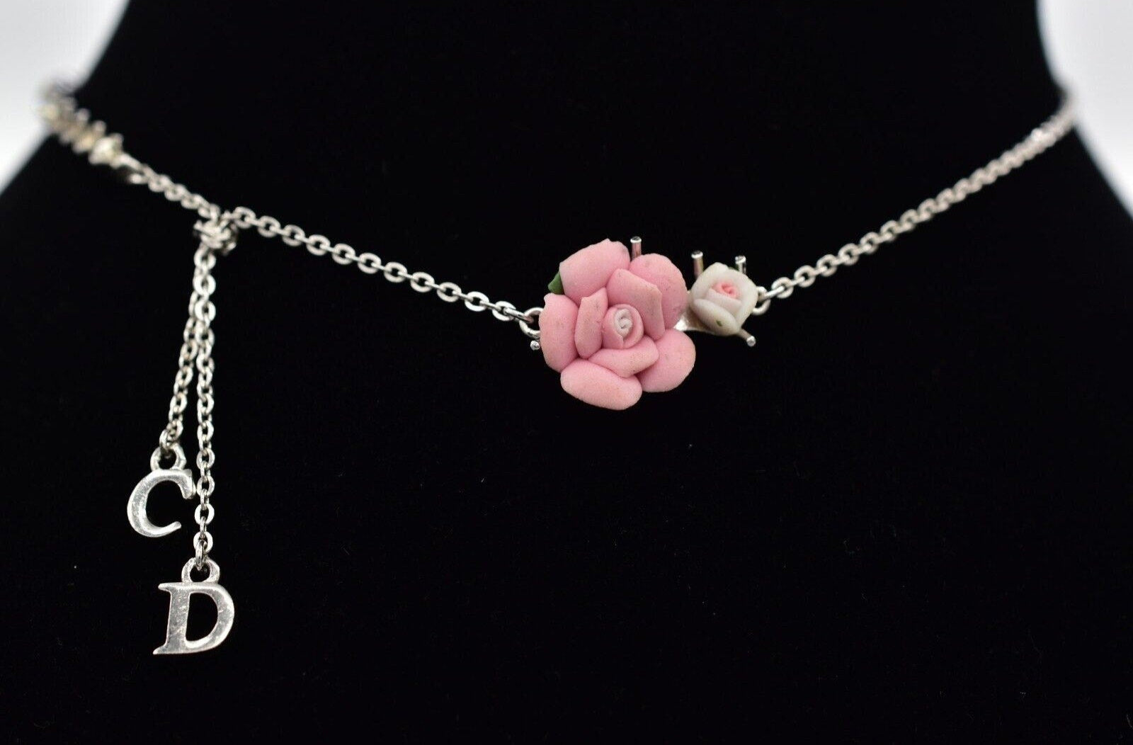 View of a vintage silver Christian Dior choker with CD charms and pink and white flowers on a black velvet neck