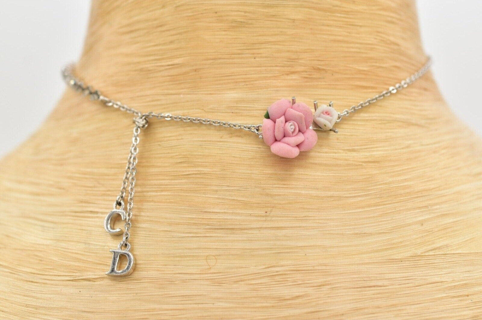 View of a vintage silver Christian Dior choker with CD charms and pink and white flowers on a white mannequin neck
