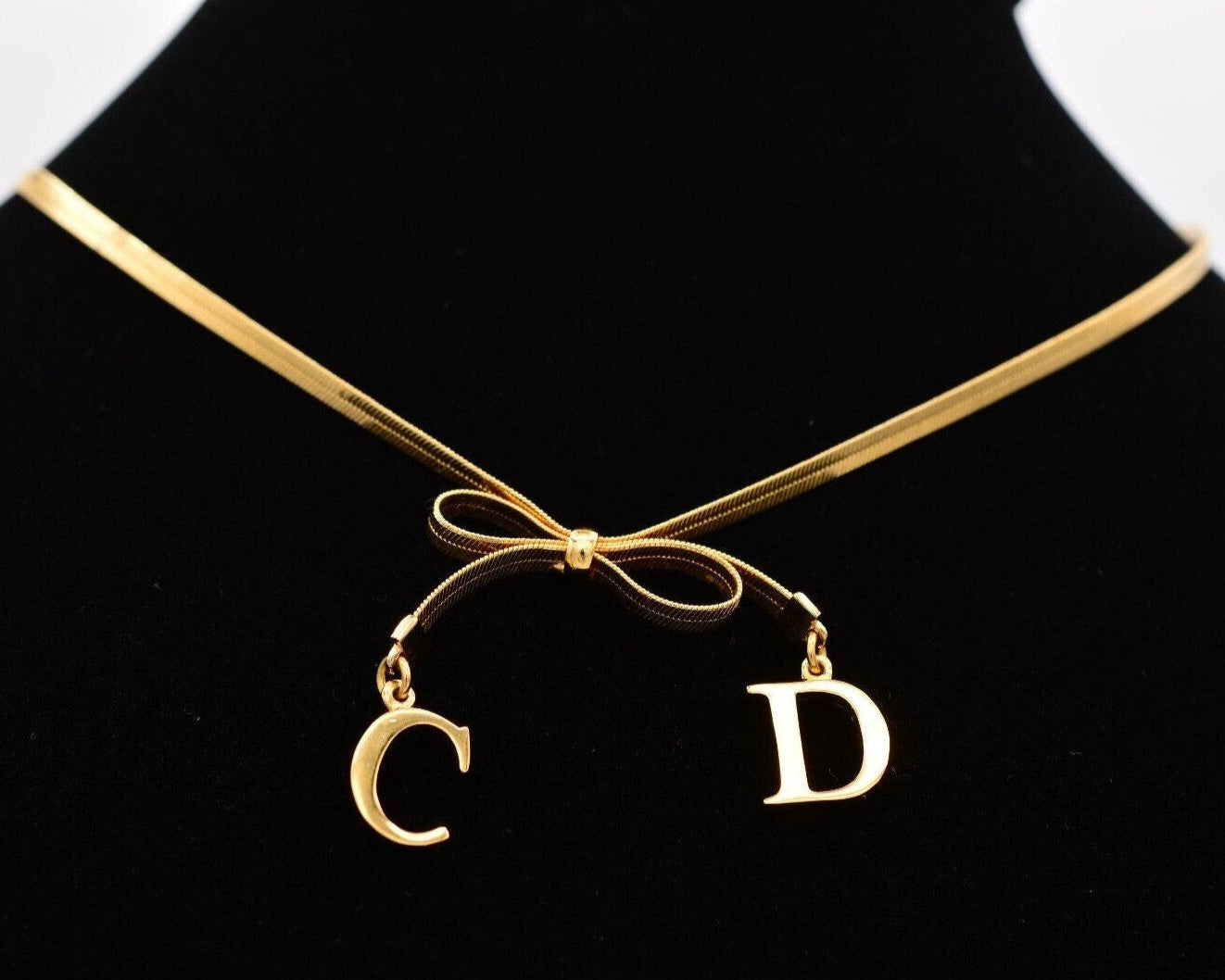 Close view of the gold dangling CD charms on a Christian Dior bow choker that is resting on a black velvet neck