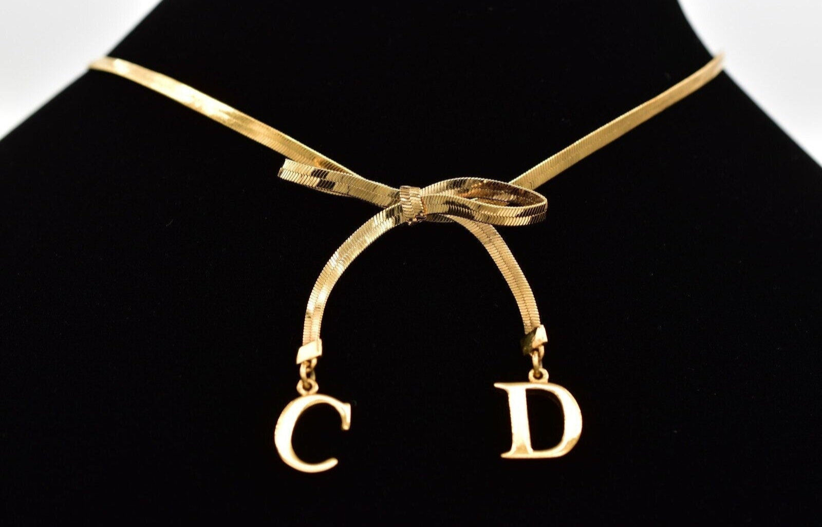 Close view of the gold dangling CD charms on a Christian Dior bow choker that is resting on a black velvet neck