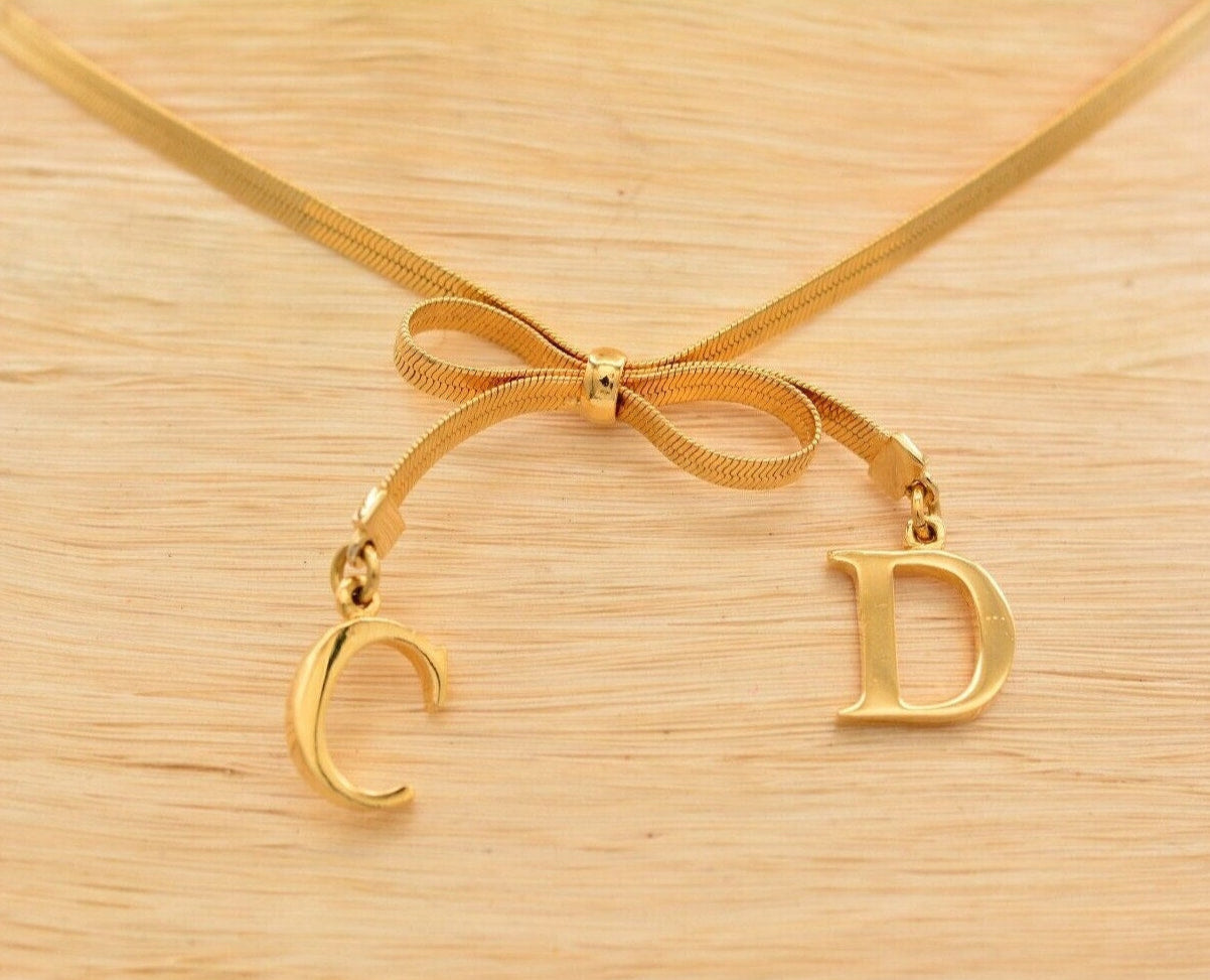 Close view of the gold dangling CD charms on a Christian Dior bow choker that is resting on a white mannequin neck