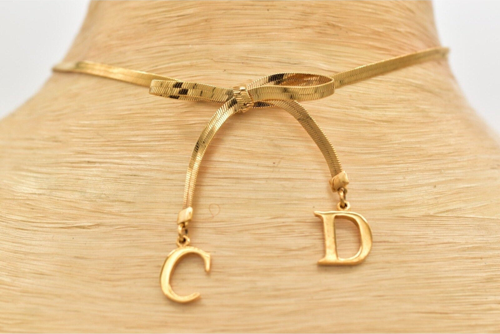 Close view of the gold dangling CD charms on a Christian Dior bow choker that is resting on a white mannequin neck