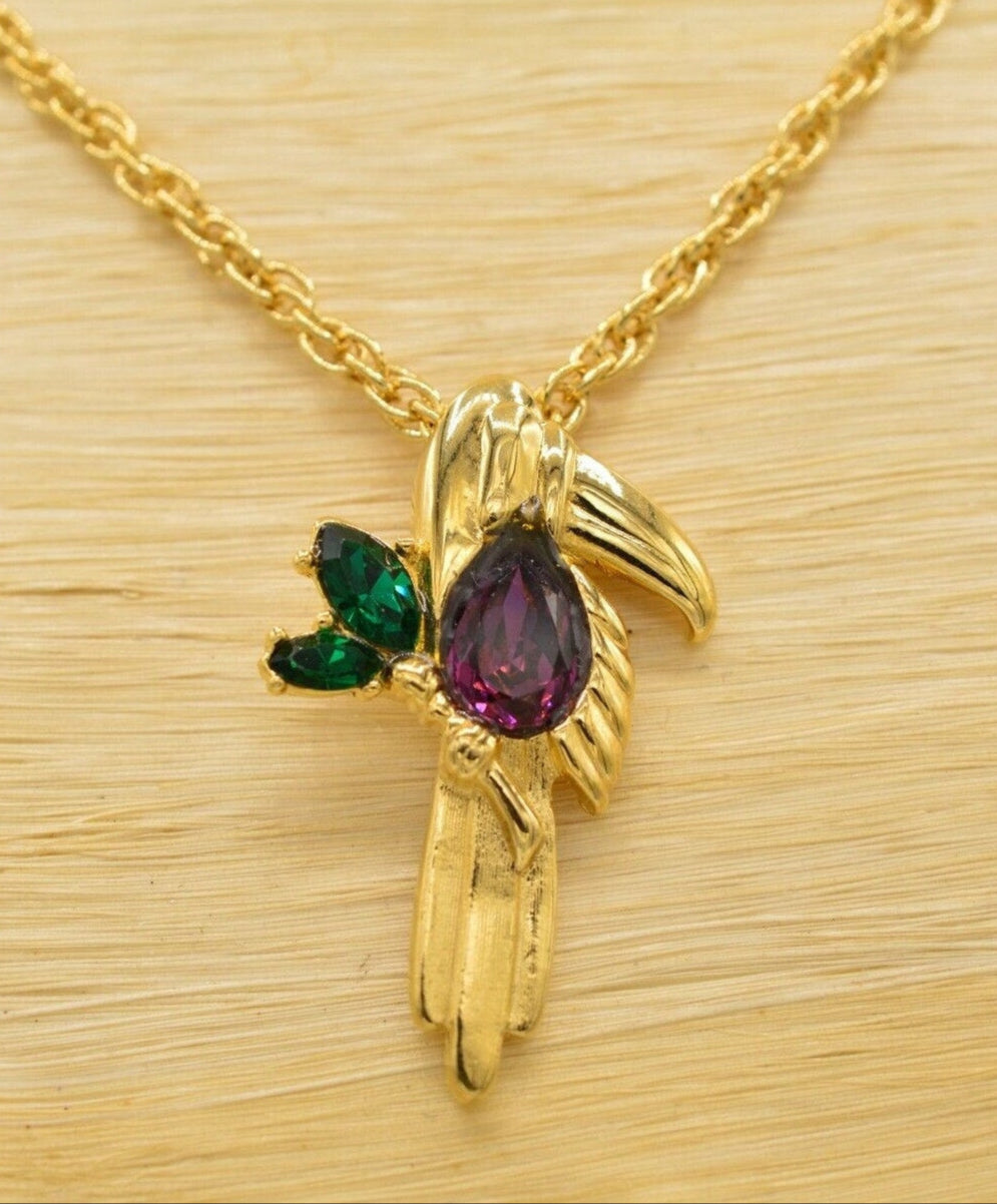 Vintage gold Givenchy chain necklace with colorful red and green crystal adorned pendant close up view on an light wooden neck