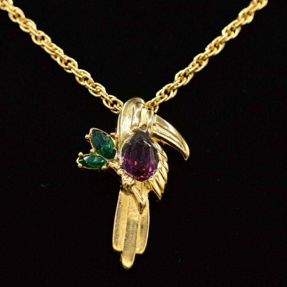 Close-up view of a vintage gold Givenchy chain necklace featuring a pendant adorned with colorful red and green crystals, resting on a black velvet neck.