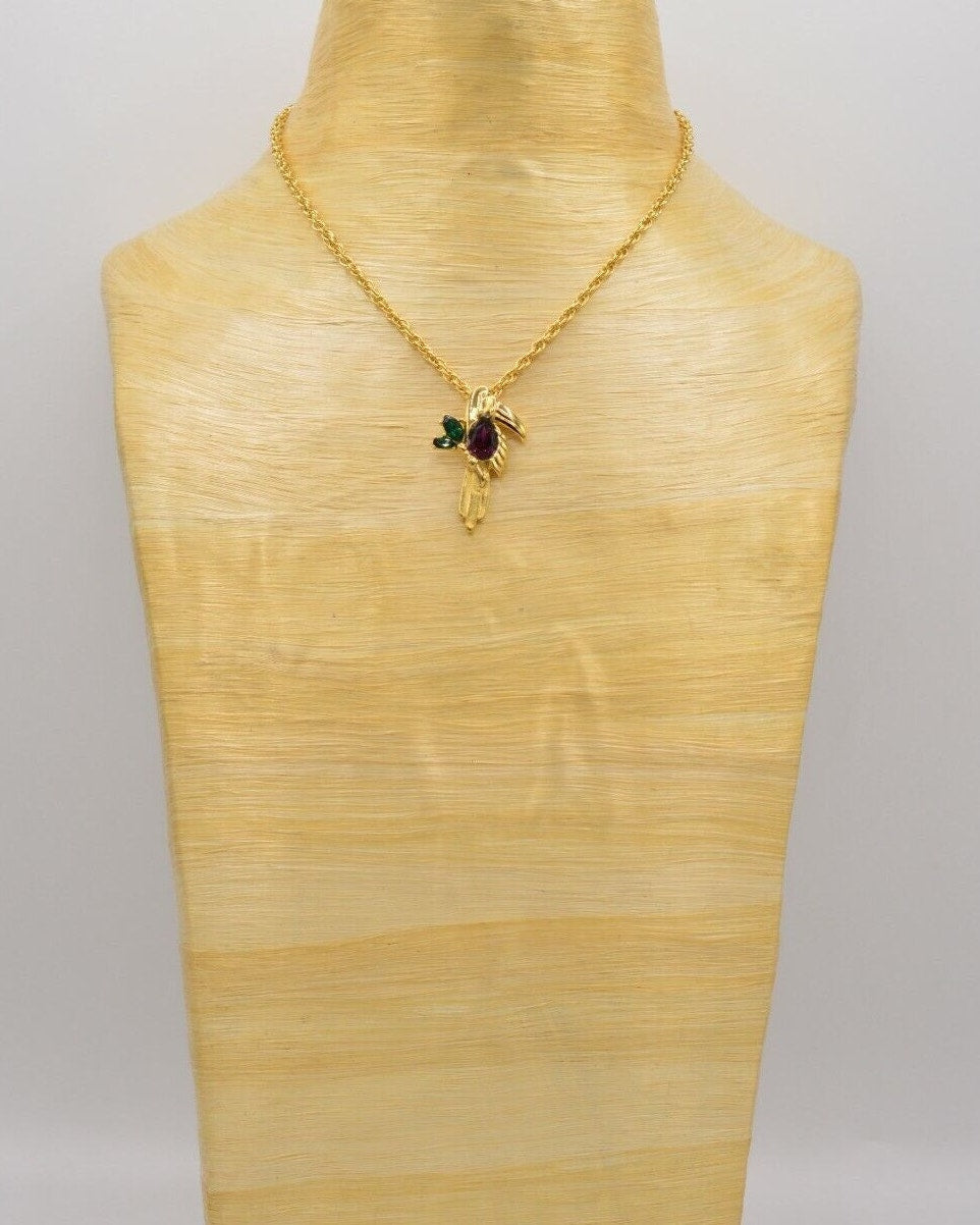 View of a vintage gold Givenchy chain necklace featuring a Toucan pendant adorned with colorful red and green crystals, resting on a light wooden neck.