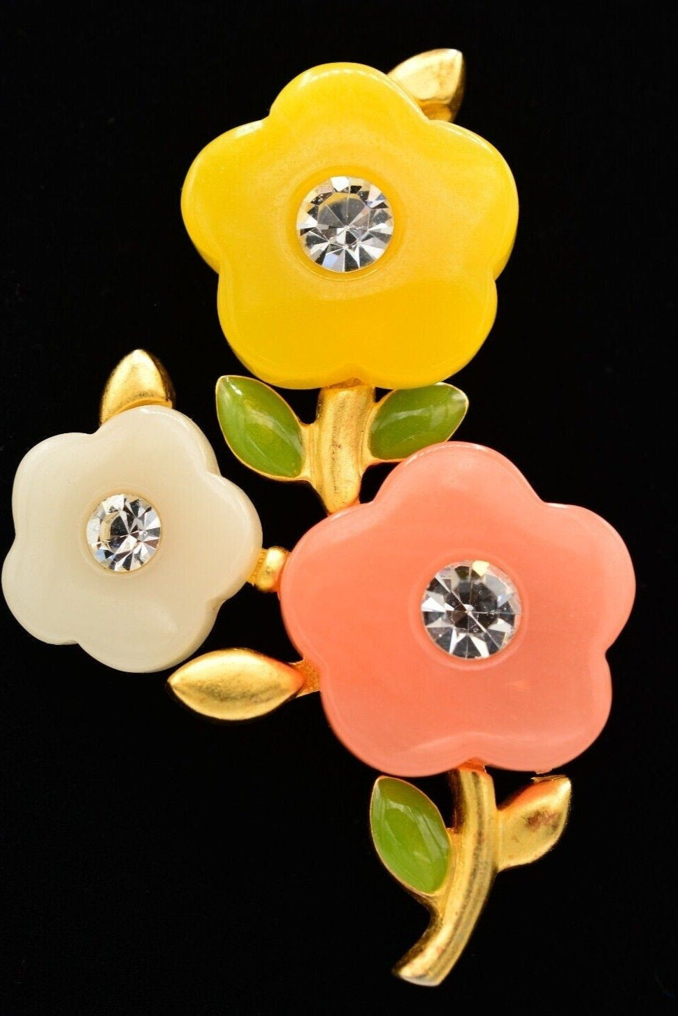 View of a vintage Givenchy brushed gold floral brooch with yellow, white, and pink colored acrylic petals with rhinestone crystals in the center on a black background